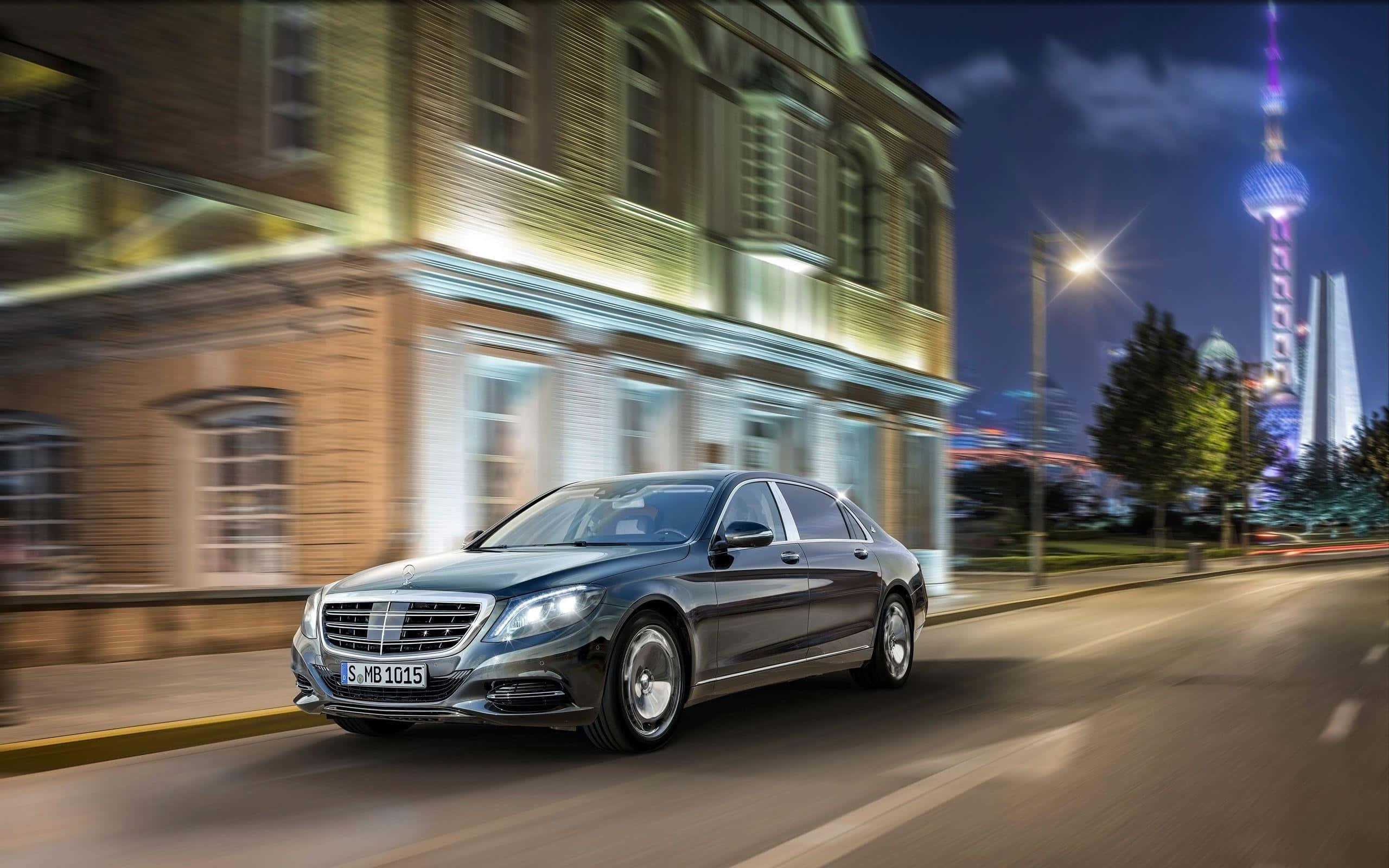 Maybach 桌布 壁紙 — 一架時尚的深灰色梅賽德斯-奔馳S級轎車在充滿活力的夜間城市景觀中疾馳，帶有模糊的動感和燈火通明的摩天大樓。