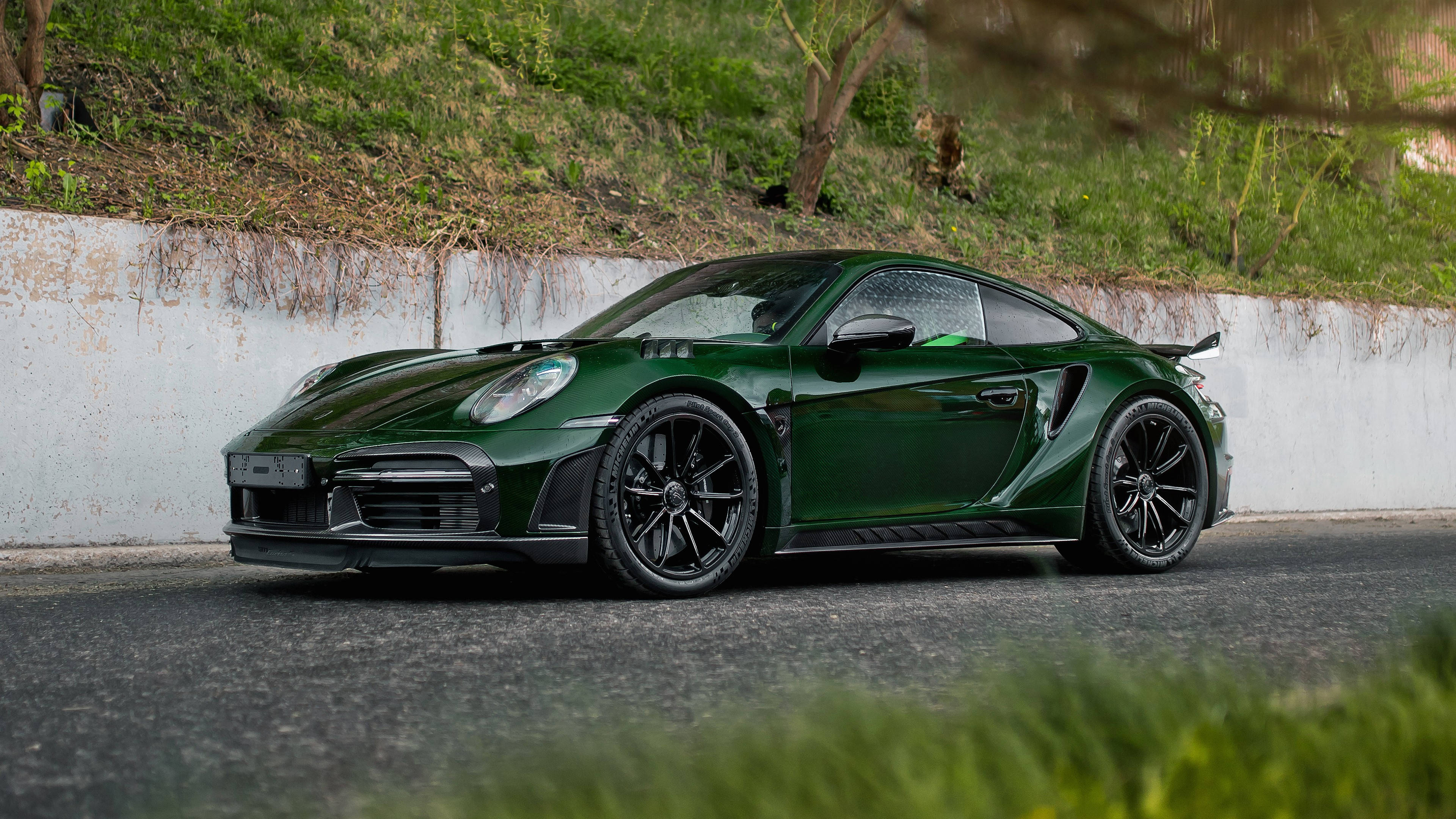保時捷 桌布 壁紙 — 一架時尚的深綠色保時捷911 GT2 RS停泊在瀝青路上，旁邊是帶有混凝土牆的草地山坡。