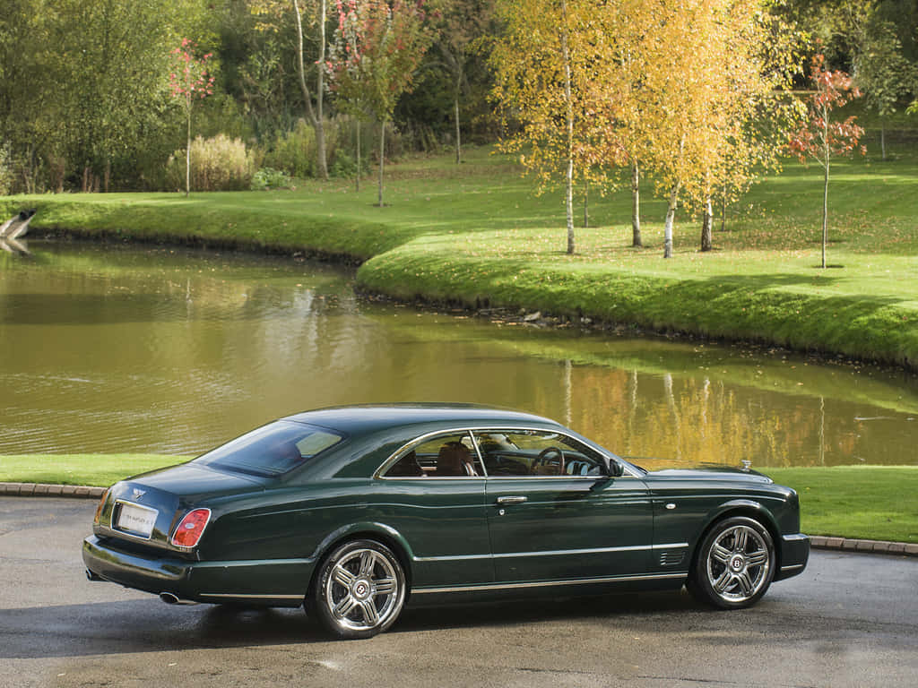Bentley Brooklands 桌布 壁紙 — 一架時尚的深綠色賓利轎跑車停在一個平靜的池塘旁，周圍是秋日金黃葉子的樹木。