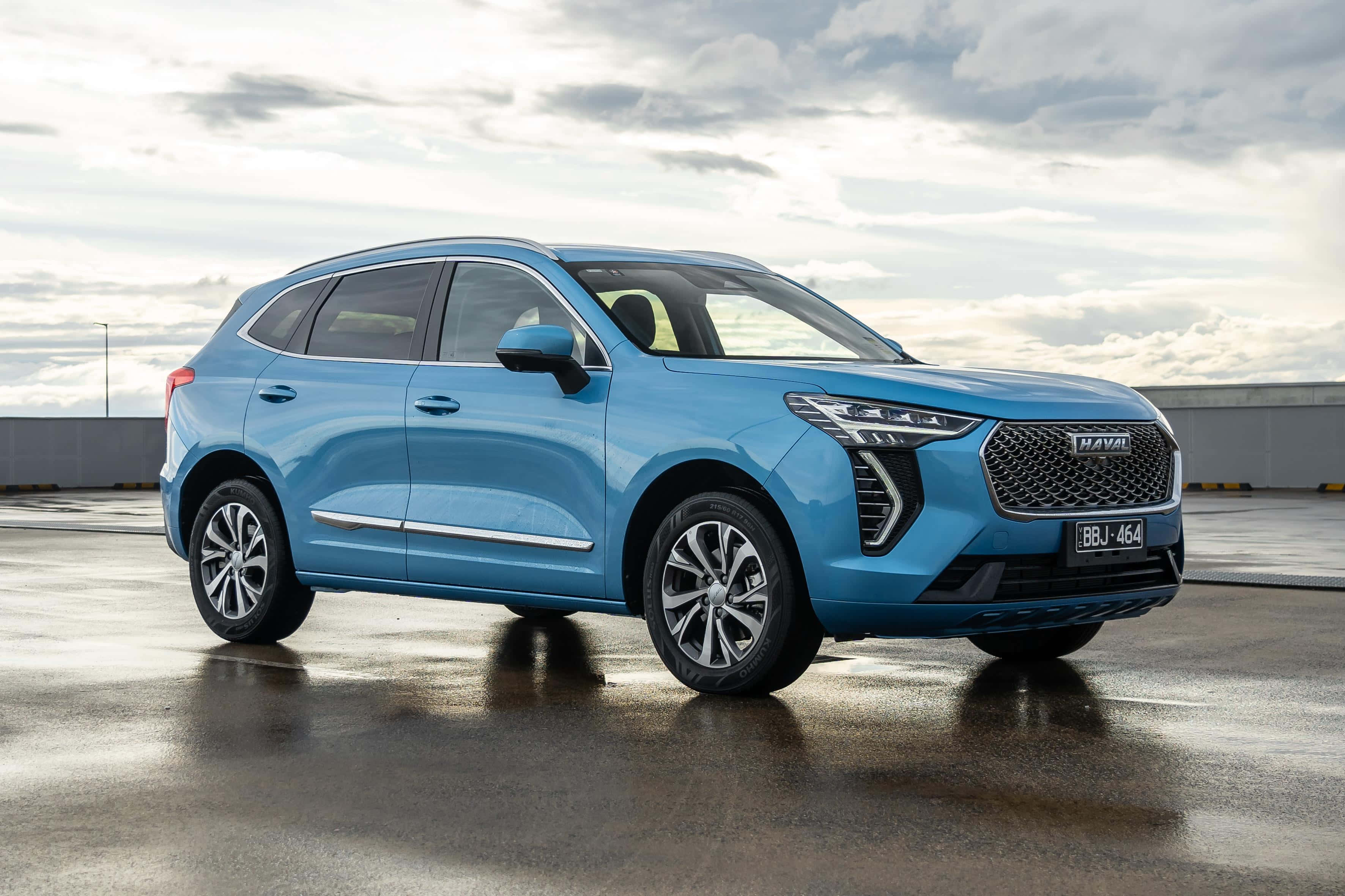 Haval 桌布 壁紙 — 一架時尚的淺藍色Haval SUV在潮濕的停車場上閃閃發光，天空多雲，倒影在路面上閃爍。