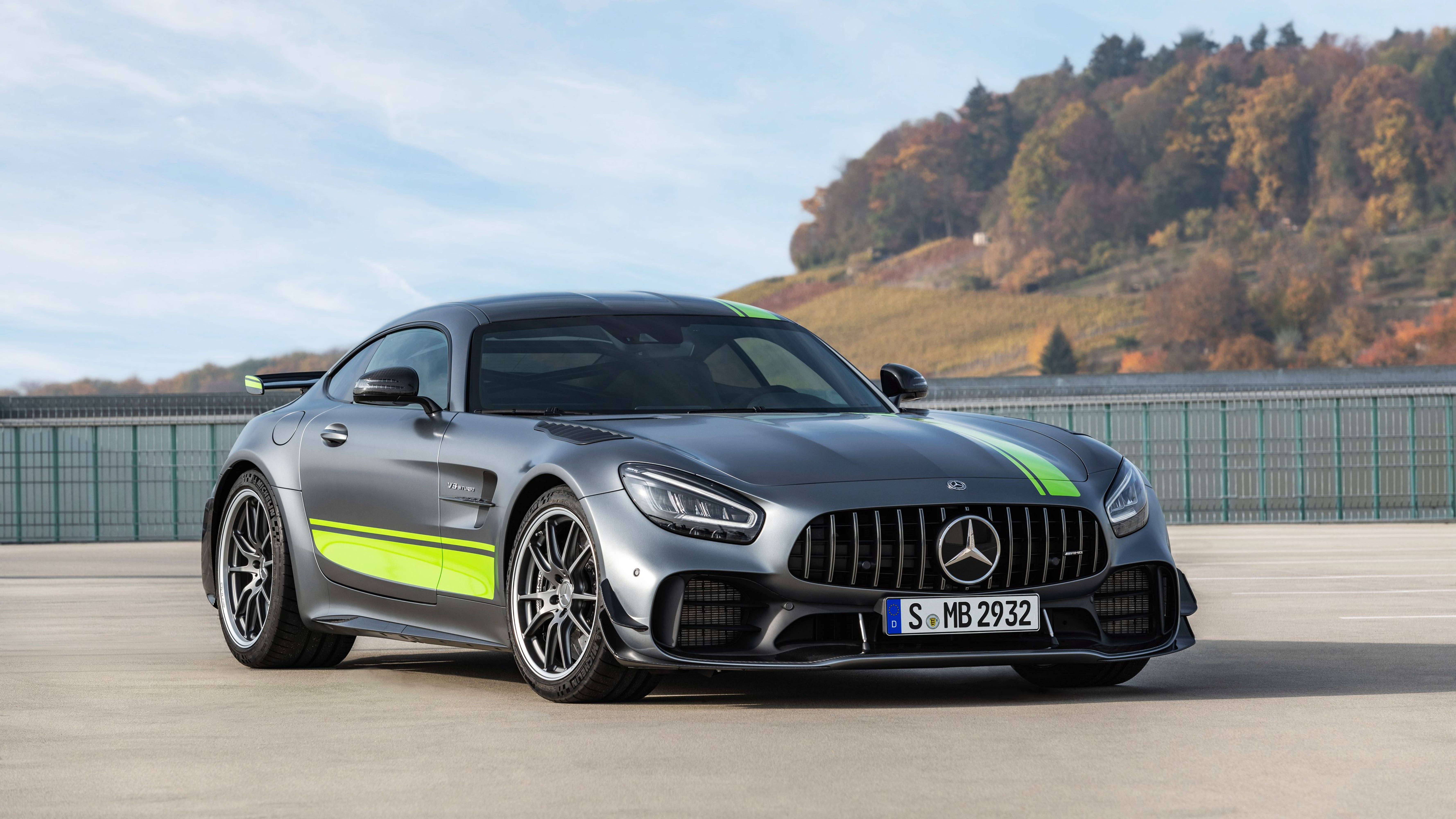 Sports Car 桌布 壁紙 — 一架時尚的灰色 Mercedes-AMG GT R 跑車，帶有螢光綠色條紋，停在混凝土賽道上，背景是秋日山丘。