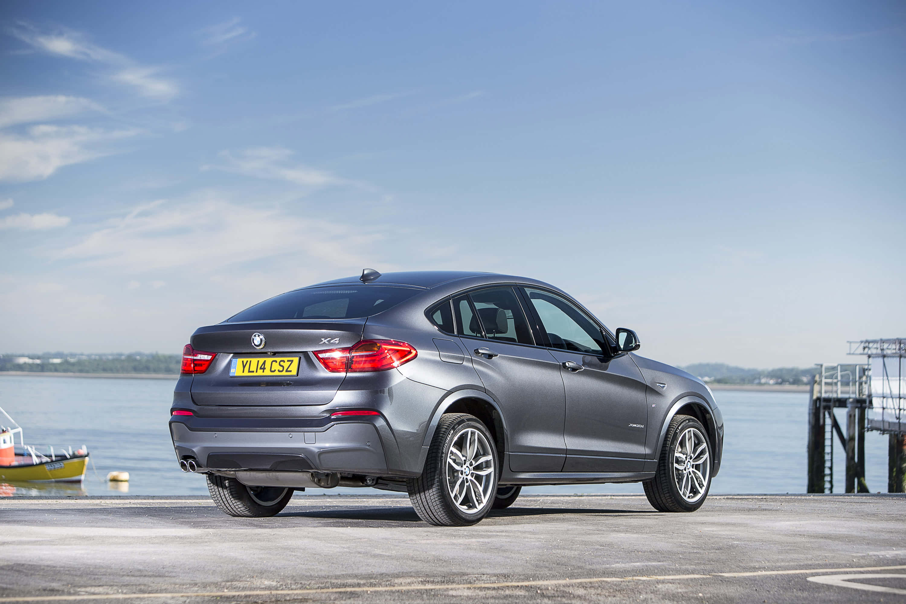Bmw X4 桌布 壁紙 — 一架時尚的灰色BMW X4 SUV停泊在海濱碼頭上，背景是平靜的海面和清澈的藍天。
