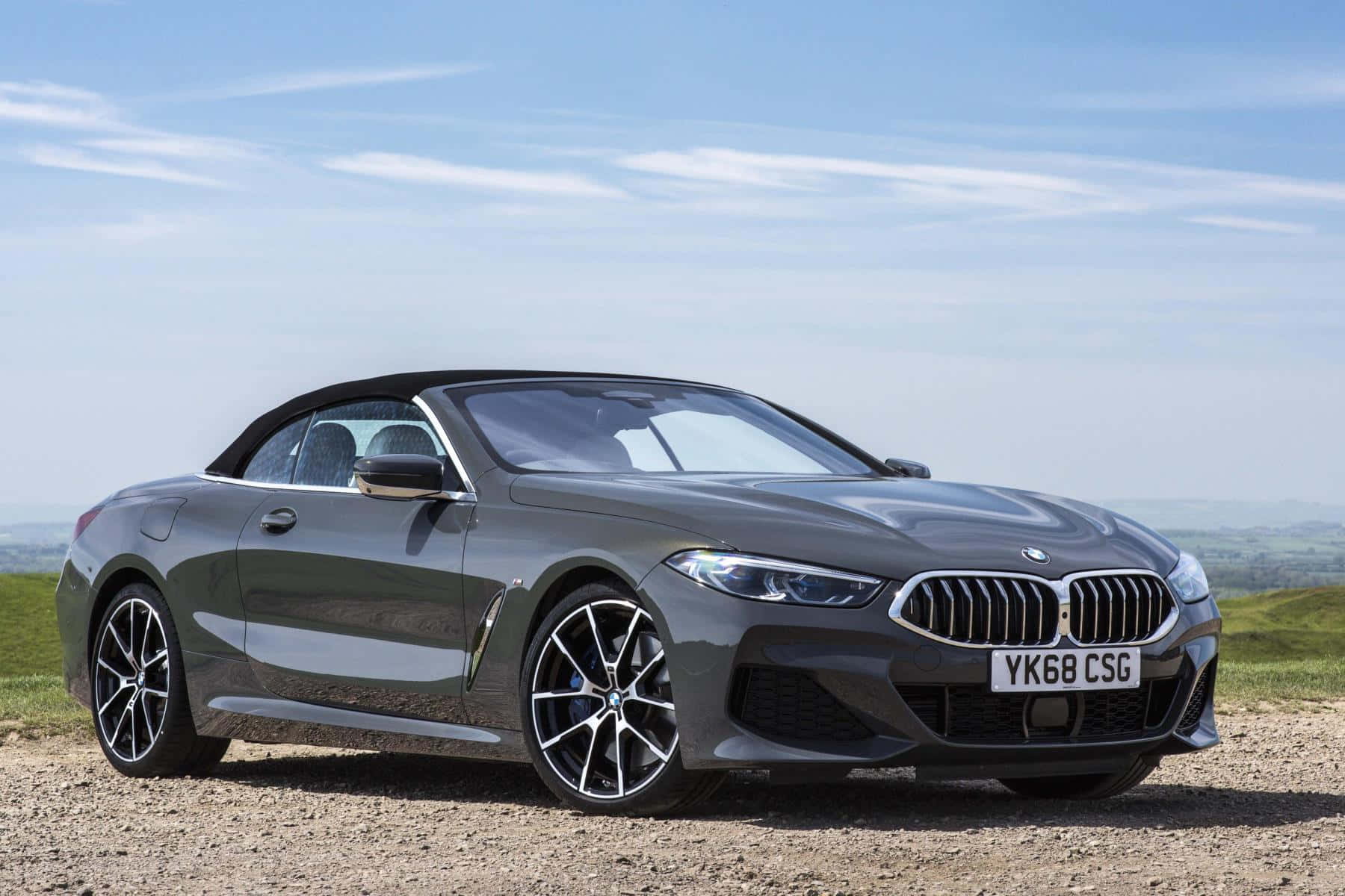 Bmw 8 Series 桌布 壁紙 — 一架時尚的灰色BMW開篷車停泊在碎石山坡上，天空湛藍，白雲點點。