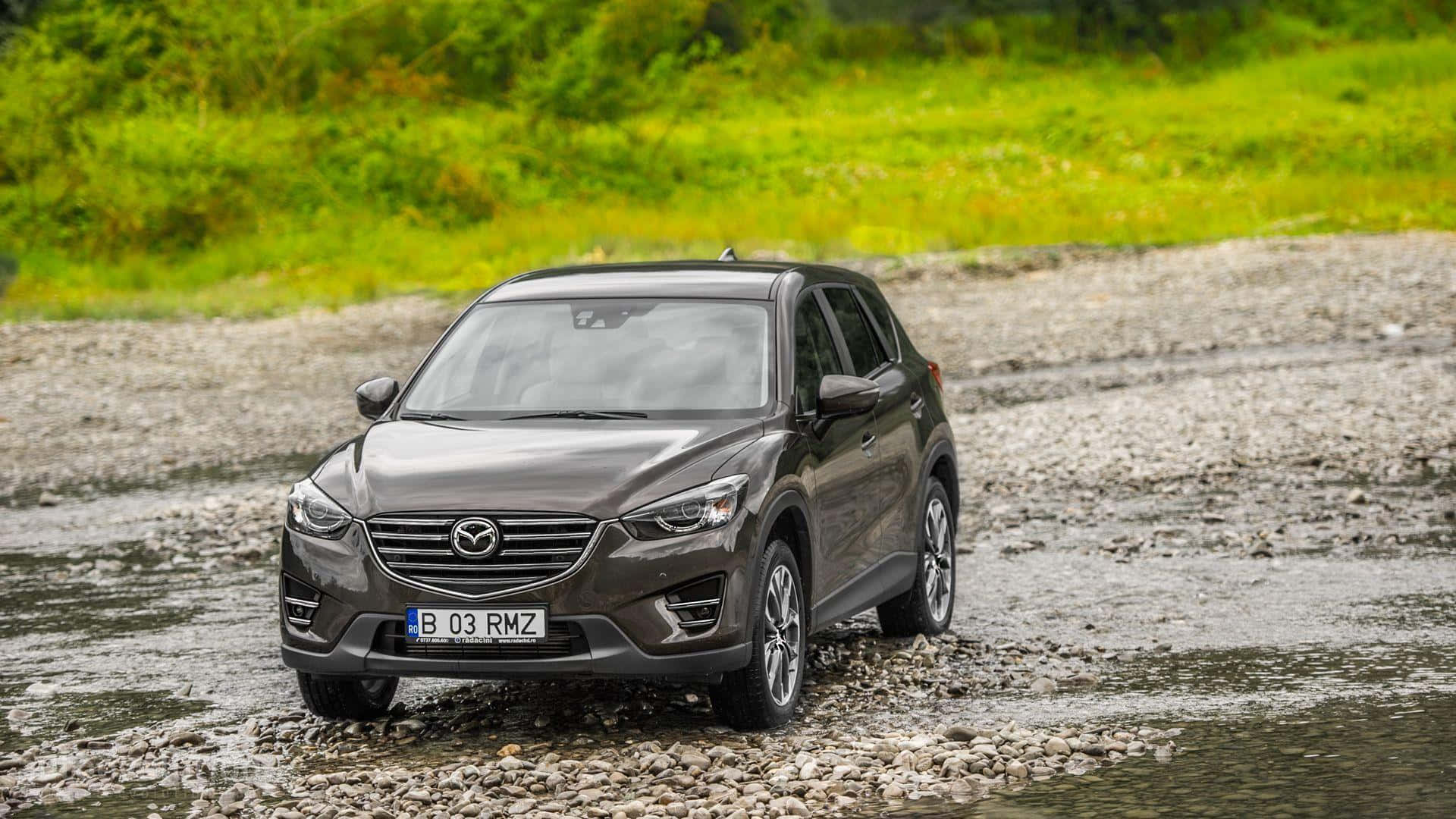 Mazda Cx-5 桌布 壁紙 — 一架時尚的灰色Mazda CX-3 SUV穿越被茂密綠草包圍的淺石溪流。
