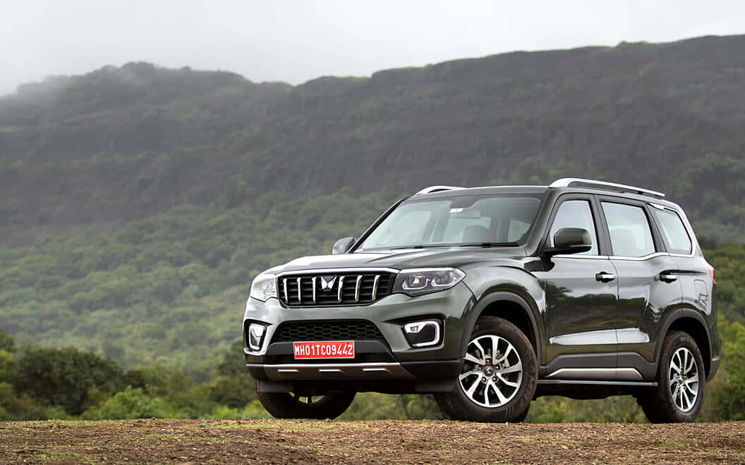 Mahindra Scorpio 桌布 壁紙 — 一架時尚的灰色SUV停泊在泥路上，背景是翠綠的山丘和霧氣繚繞的山脈。
