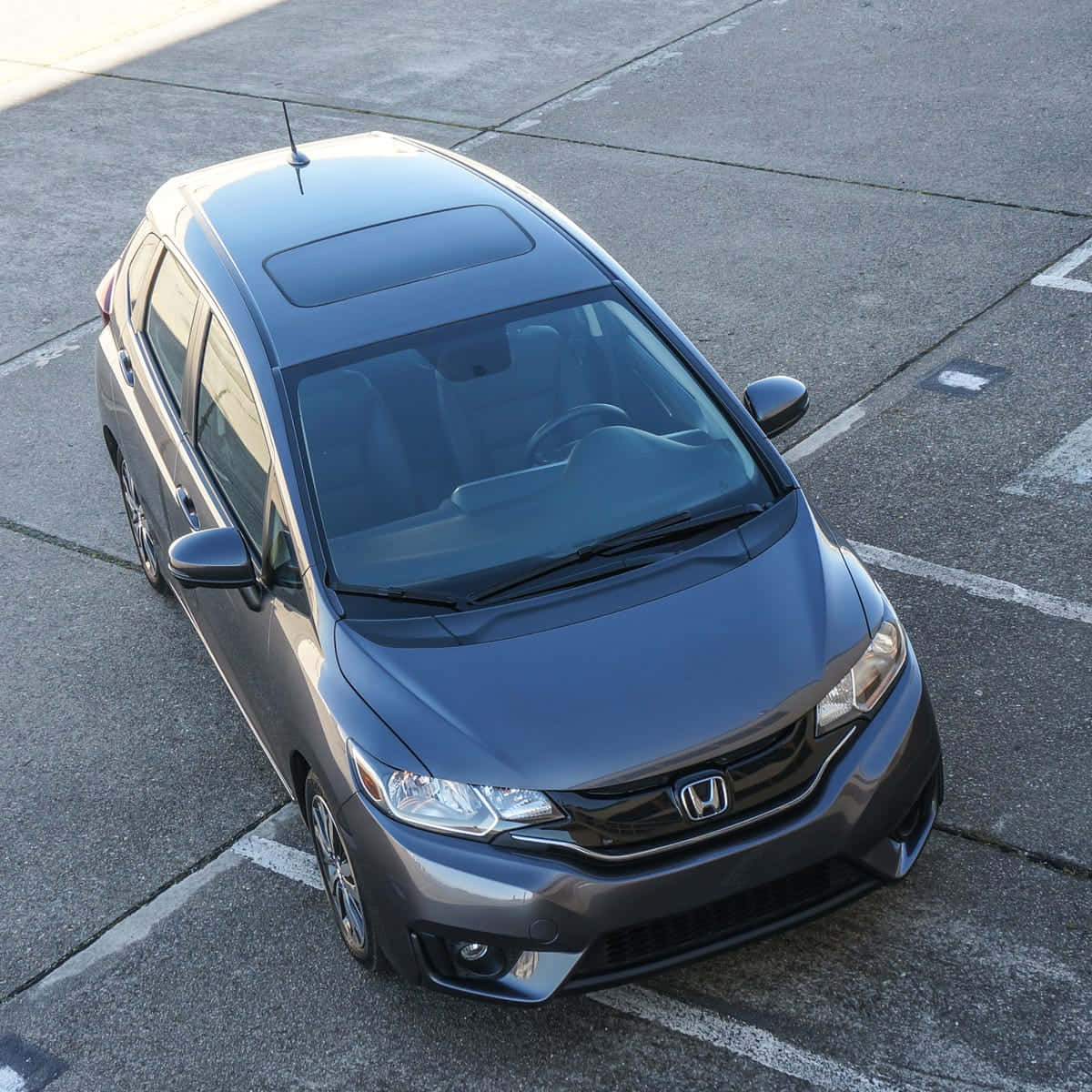 Honda Fit 桌布 壁紙 — 一架時尚的灰色本田Fit停泊在陽光普照的混凝土停車場，地上有白色標線。