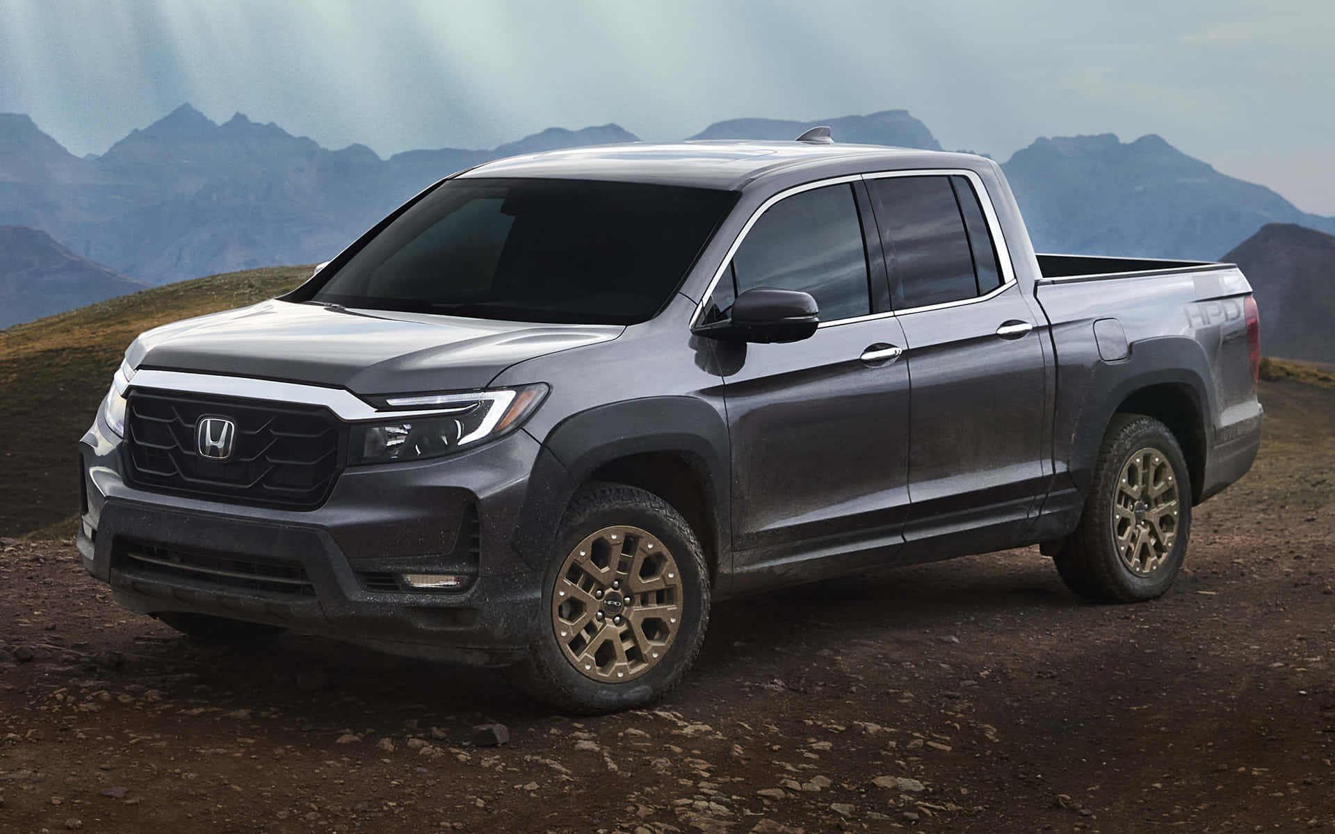 Honda Ridgeline 桌布 壁紙 — 一架時尚的灰色本田皮卡車停在崎嶇的泥路上，背景是霧濛濛的山巒。