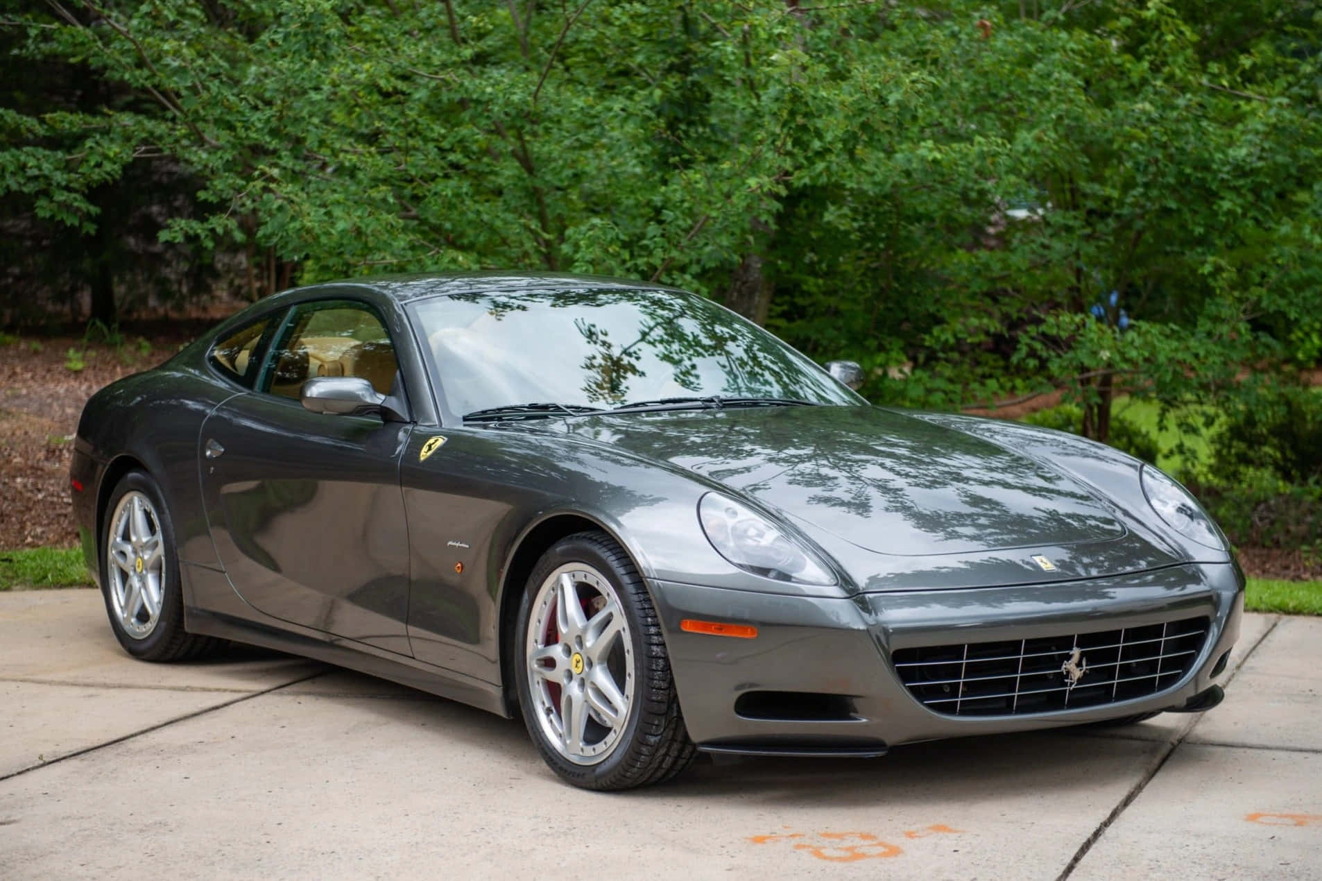 Ferrari 612 Scaglietti 桌布 壁紙 — 一架時尚的灰色法拉利 612 Superamerica 停泊在混凝土車道上，周圍環繞著茂密的綠樹。
