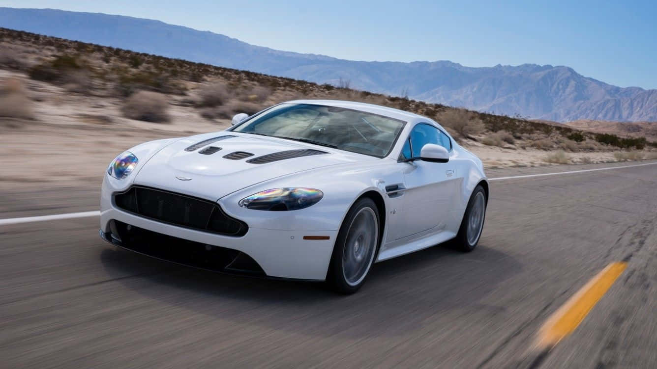 Aston Martin V12 Vantage 桌布 壁紙 — 一架時尚的白色Aston Martin在沙漠公路上疾馳，背景是山脈，天空湛藍清澈。