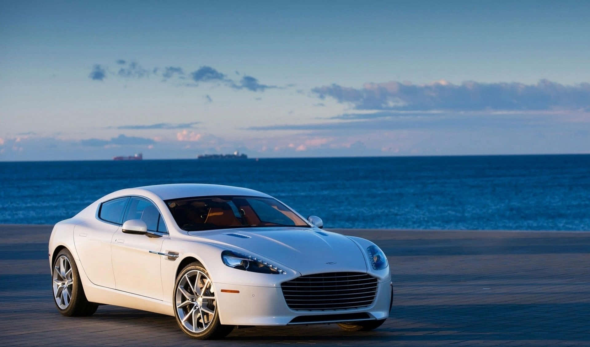 Aston Martin Rapide S 桌布 壁紙 — 一架時尚的白色Aston Martin跑車停泊在暮色中的海濱長廊，背景是海洋和遠處的船隻。