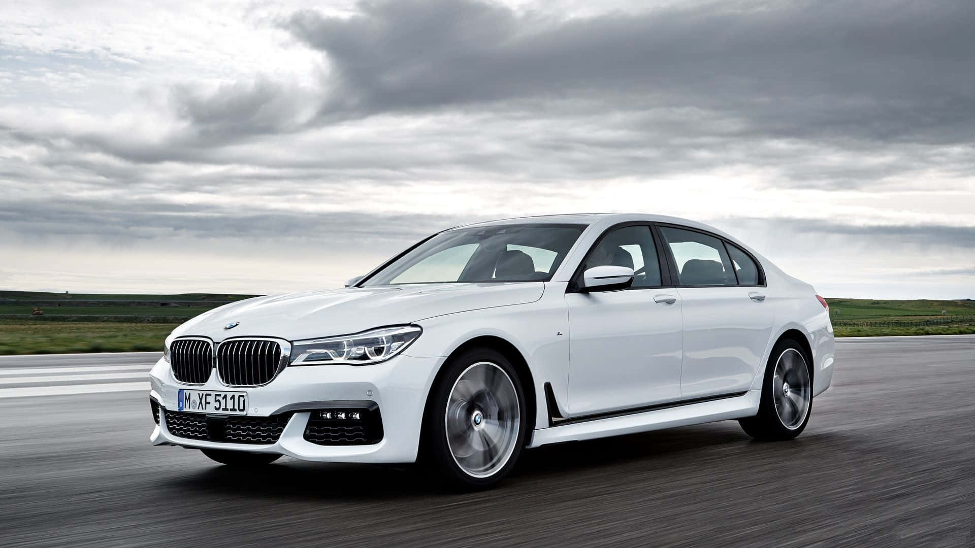 Bmw 7 Series 桌布 壁紙 — 一架時尚的白色BMW 7系轎車在戲劇性的多雲天空下高速行駛在高速公路上。
