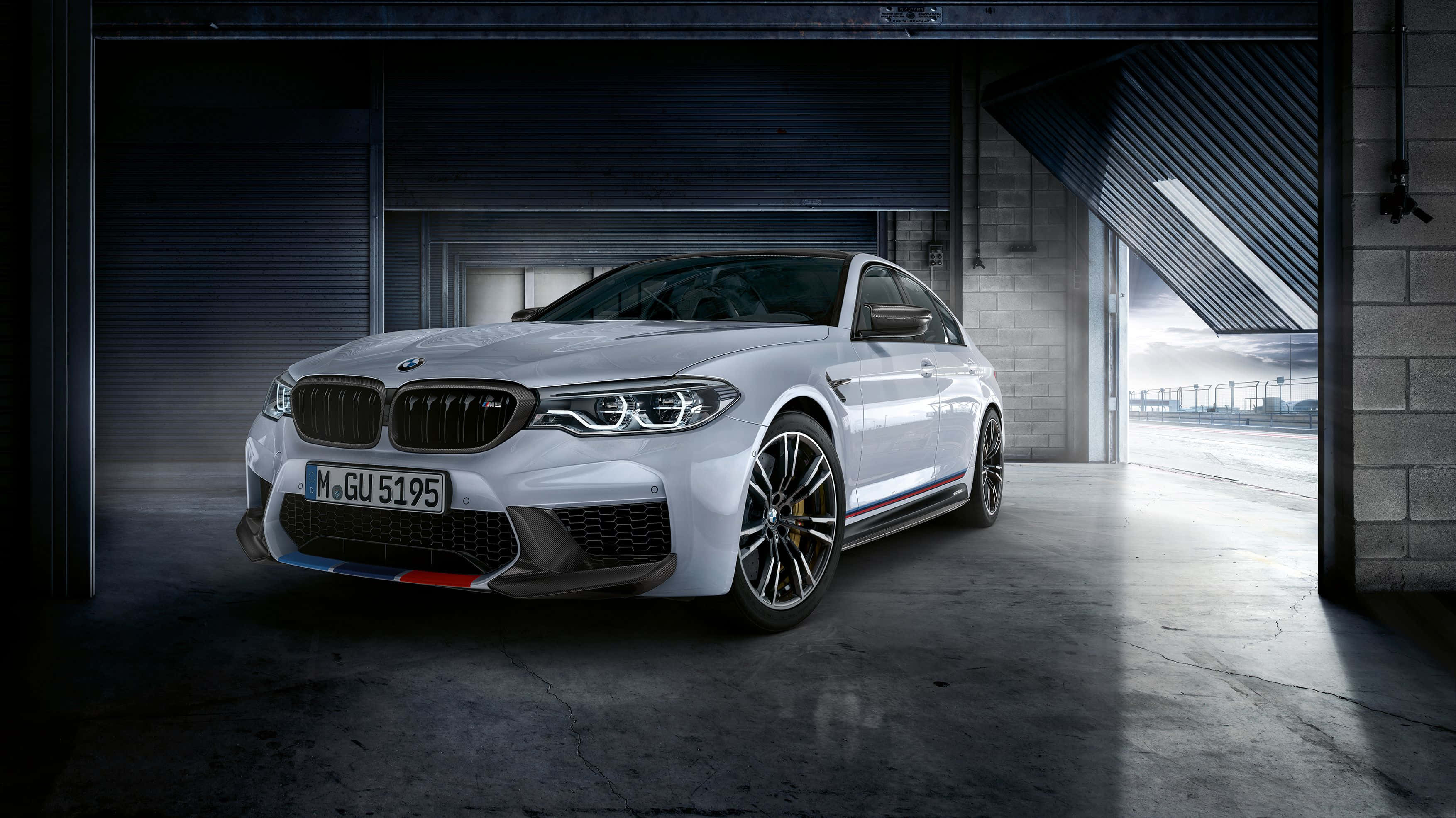 Bmw M5 桌布 壁紙 — 一架時尚的白色BMW M5停泊在昏暗的工業車庫中，戲劇性的燈光突顯其侵略性設計。