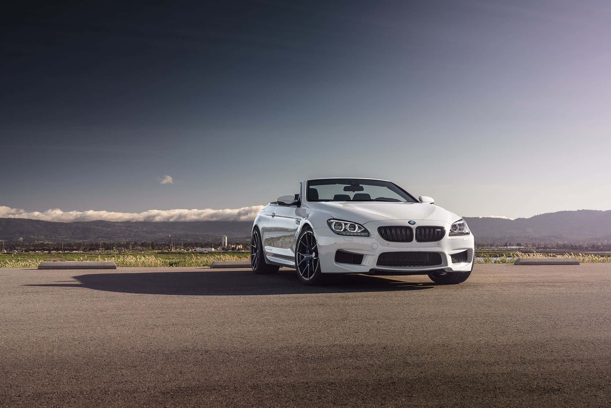 Bmw M6 桌布 壁紙 — 一架時尚的白色BMW M6開篷車停泊在瀝青路上，背景是晴朗天空下的遠山和白雲。