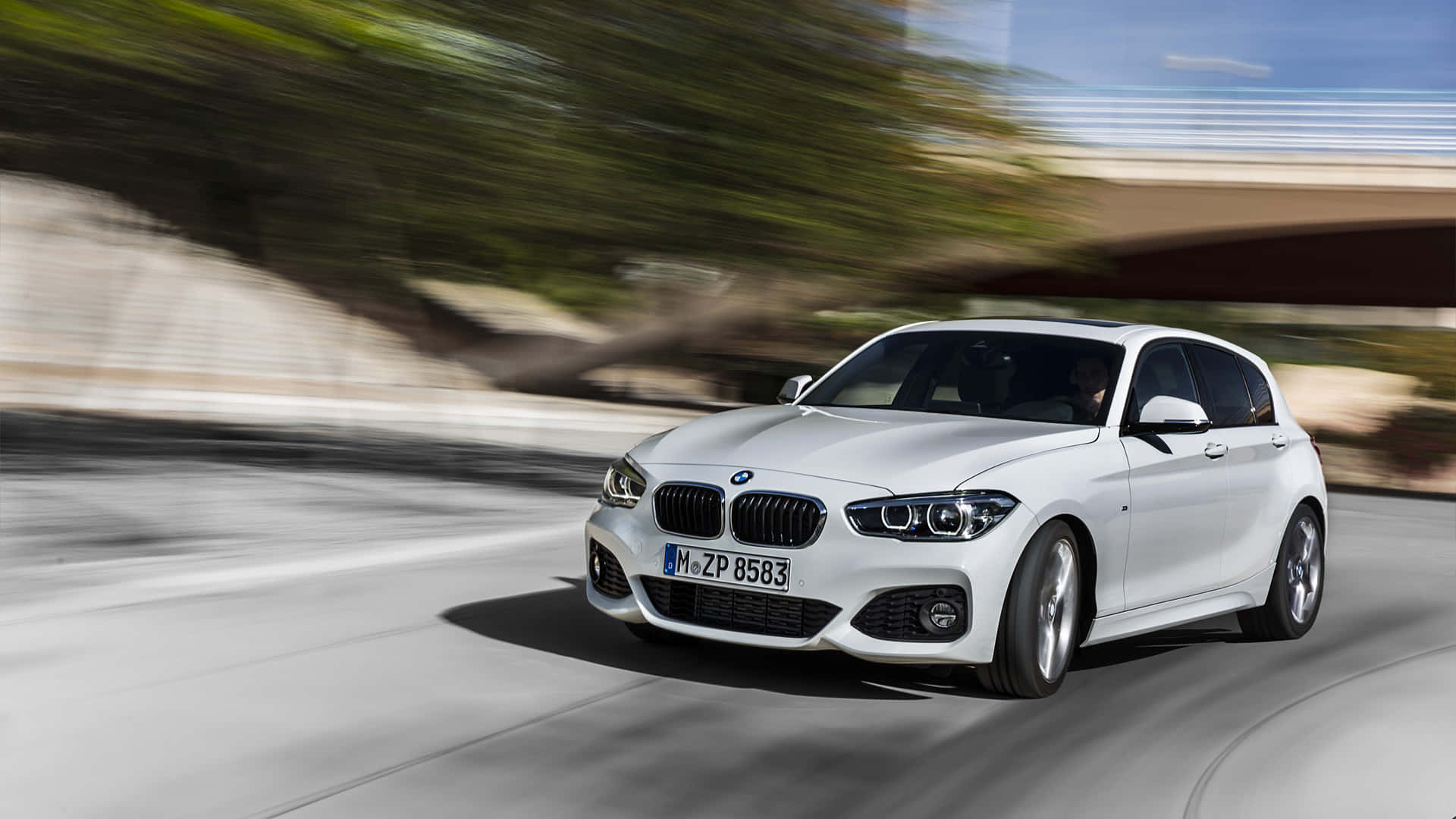 Bmw 1 Series 桌布 壁紙 — 一架時尚的白色BMW掀背車沿著彎曲的道路疾馳，上方有模糊的綠化和混凝土橋樑。
