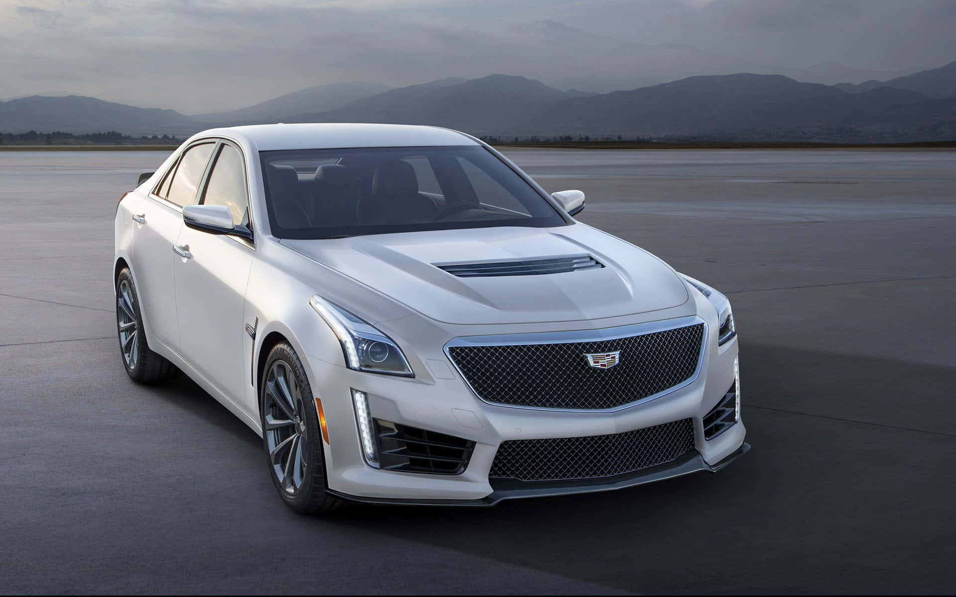 Cadillac Cts 桌布 壁紙 — 一架時尚的白色Cadillac CTS-V運動轎車停泊在廣闊的混凝土場地上，遠山在陰天之下。