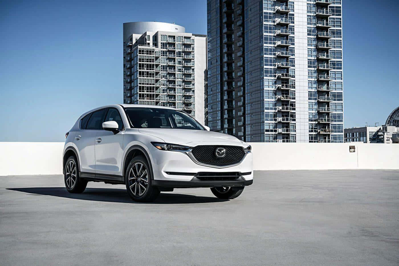 Mazda Cx-5 桌布 壁紙 — 一架時尚的白色Mazda CX-5 SUV停泊在天台上，背後是現代化的玻璃摩天大樓，在清澈的藍天下高聳入雲。