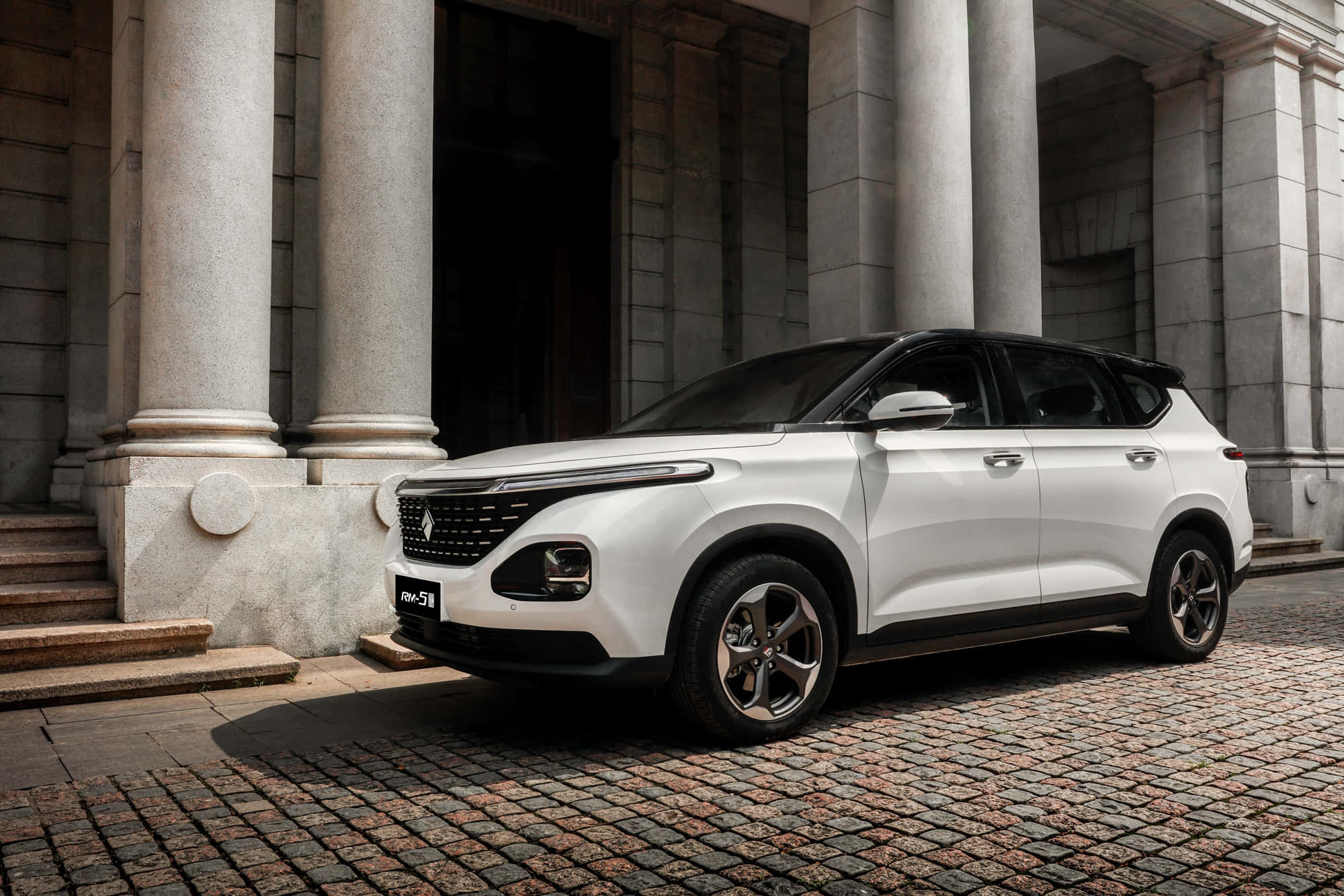 Baojun 桌布 壁紙 — 一架時尚的白色SUV停泊在鵝卵石街道上，前方是宏偉的石柱建築。