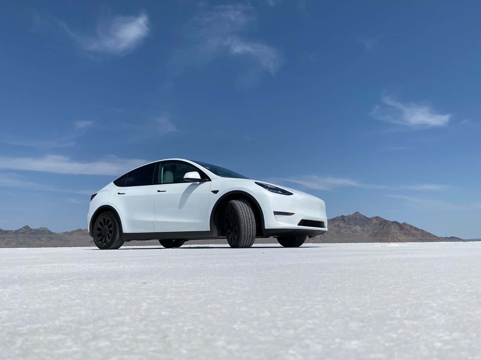 tesla 桌布 壁紙 — 一架時尚的白色Tesla Model Y獨自停泊在廣闊的鹽灘上，背景是晴朗的藍天和遠山。