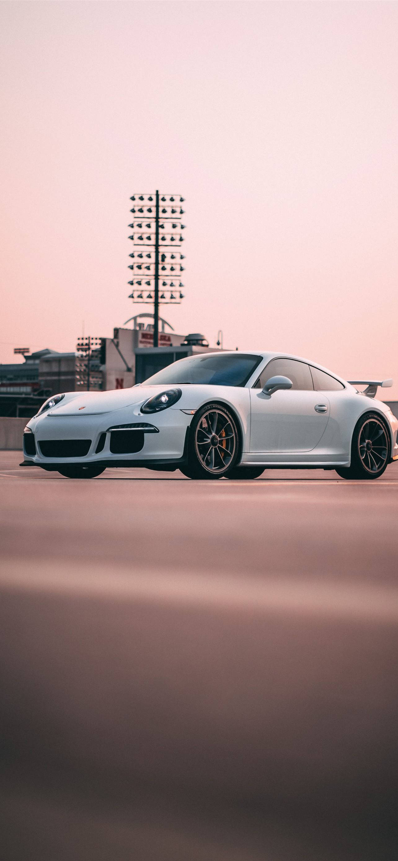 保時捷 桌布 壁紙 — 一架時尚的白色保時捷911 GT3 RS在日落時停泊在賽道上，背景有體育場燈光。