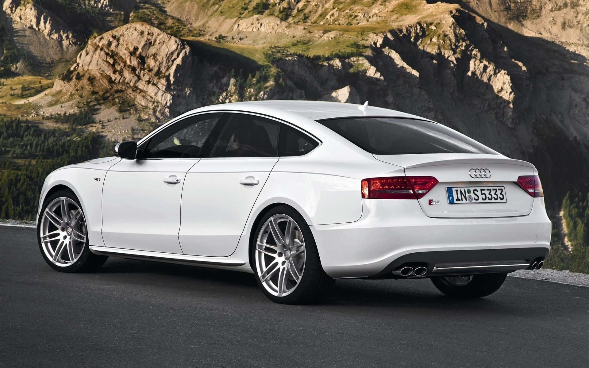 Audi S5 桌布 壁紙 — 一架時尚的白色奧迪房車停泊在山路上，背景是崎嶇的懸崖和綠意。