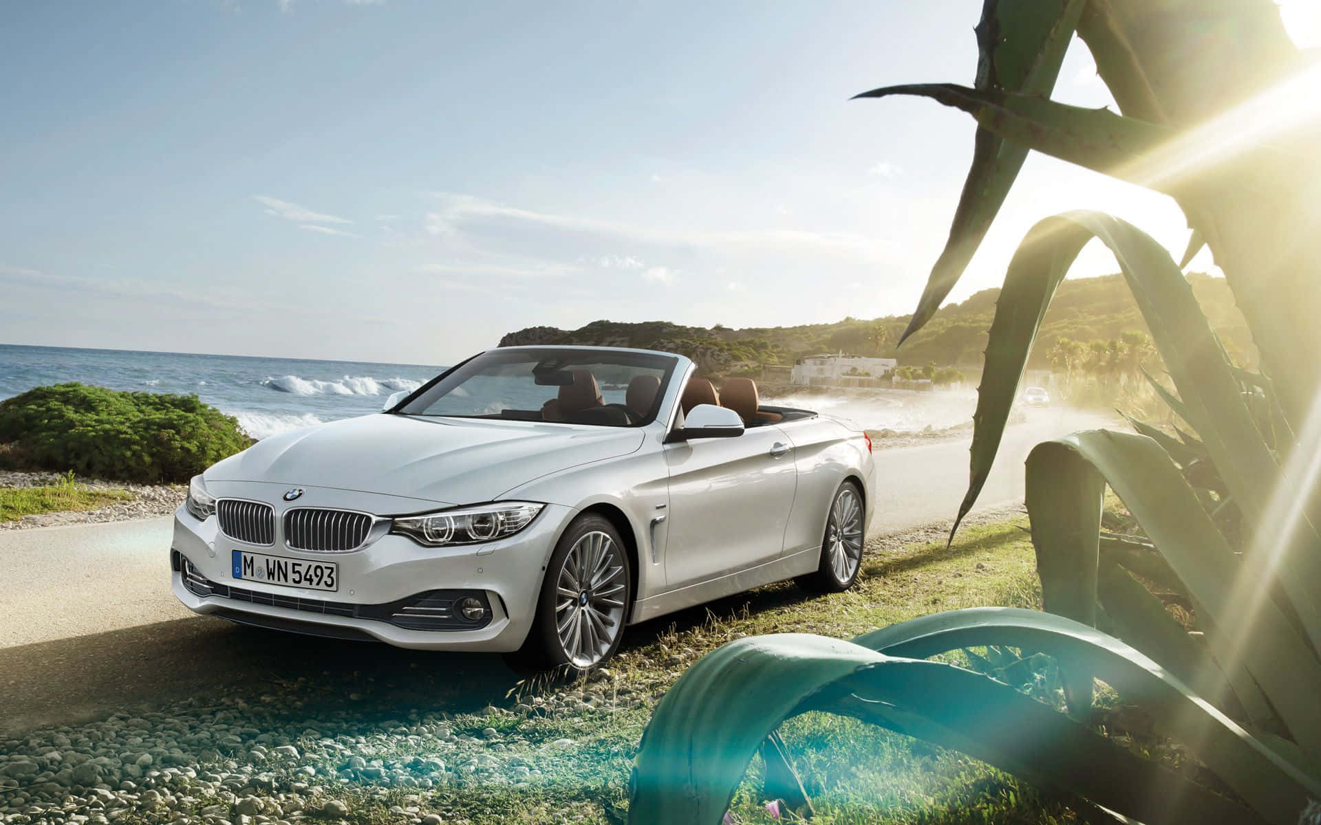 Bmw 4 Series 桌布 壁紙 — 一架時尚的白色寶馬開篷車停泊在沿海公路上，附近有海浪拍打，陽光穿過熱帶樹葉灑落。