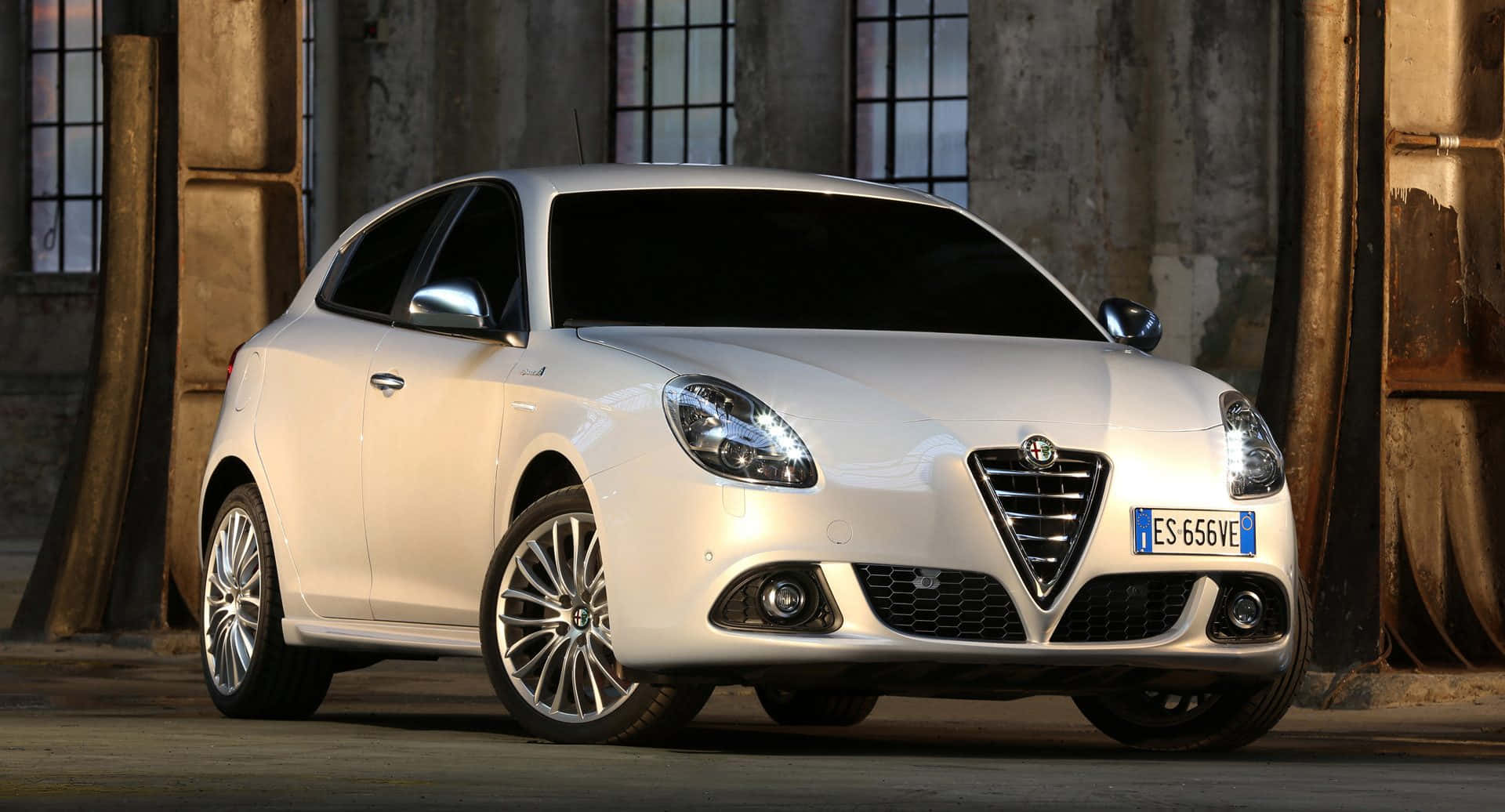 Alfa Romeo Giulietta 桌布 壁紙 — 一架時尚的白色愛快羅密歐Giulietta停泊在溫暖燈光的鄉村工業環境中。