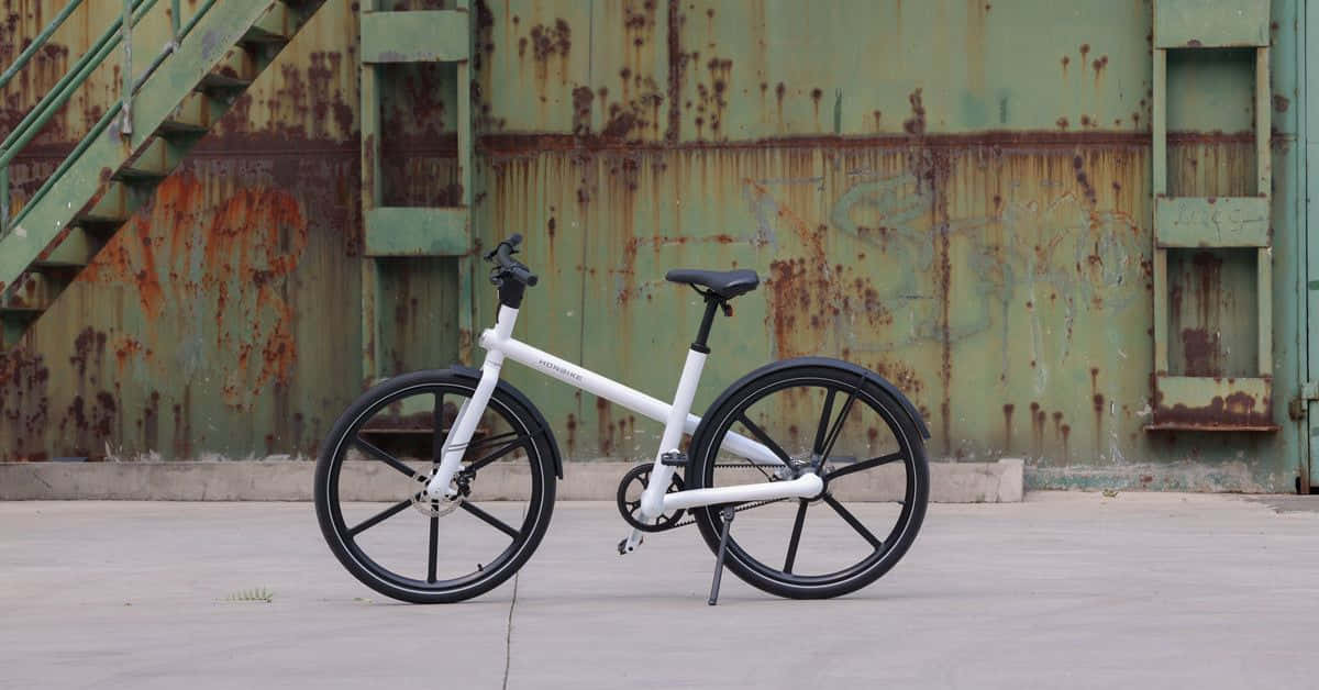 Electric Bike 桌布 壁紙 — 一架時尚的白色摺疊單車，靠著一道帶樓梯的風化綠色鏽蝕金屬牆。
