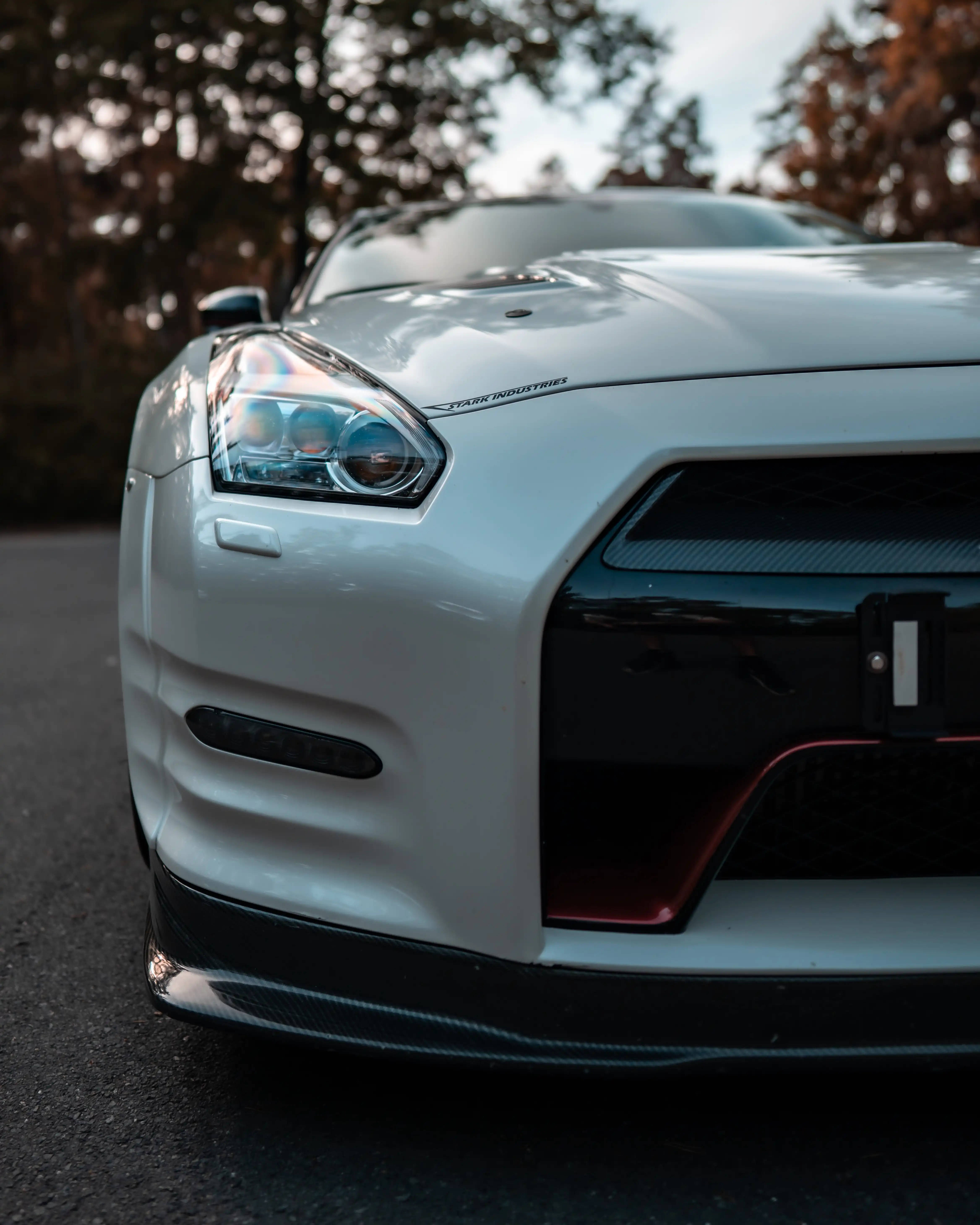 Nissan 桌布 壁紙 — 一架時尚的白色日產GT-R跑車，帶有碳纖維飾邊和紅色飾條，停在秋天的樹下的瀝青路上。