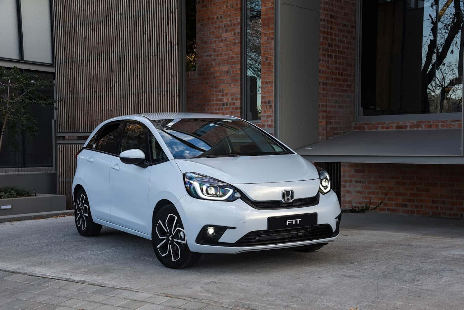 Honda Fit 桌布 壁紙 — 一架時尚的白色本田Fit停泊在鋪砌的庭院旁，旁邊是一座現代磚木建築。