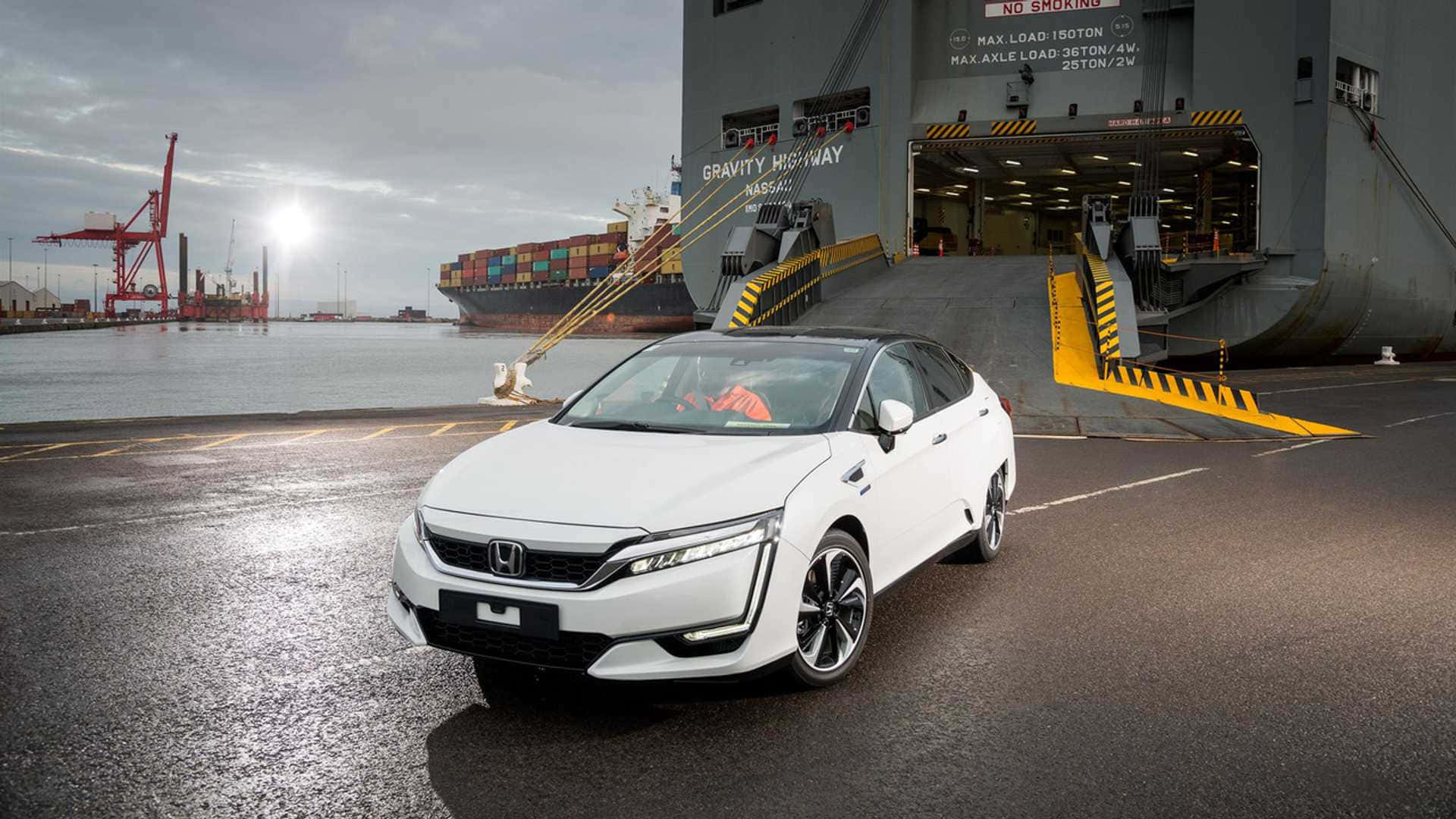 Honda Clarity 桌布 壁紙 — 一架時尚的白色本田房車停泊在濕滑的碼頭上，旁邊是一艘巨大的貨船，背景有起重機，天空多雲。