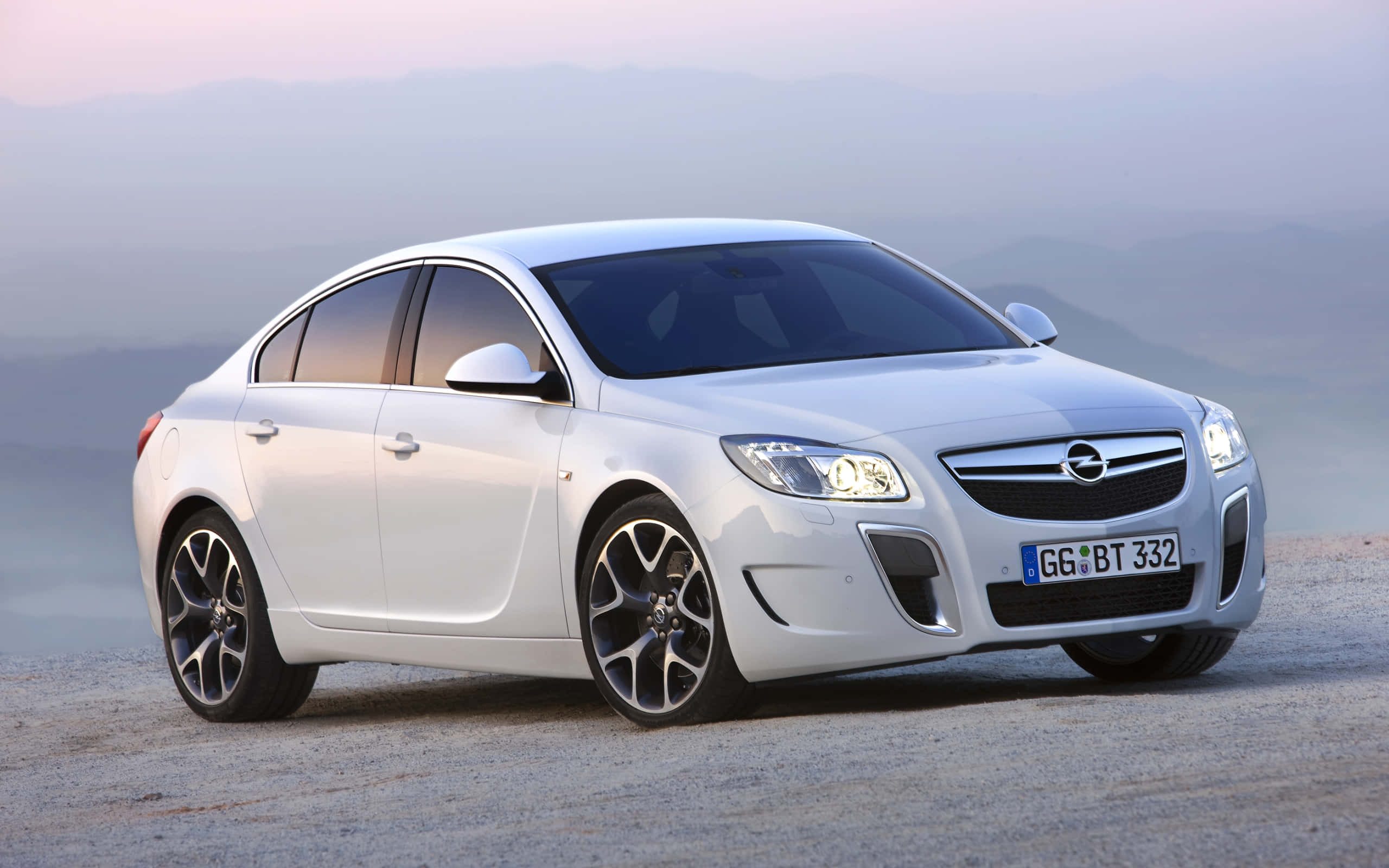 Opel Insignia 桌布 壁紙 — 一架時尚的白色歐寶Insignia停泊在碎石路上，背景是黎明時分朦朧的山巒。