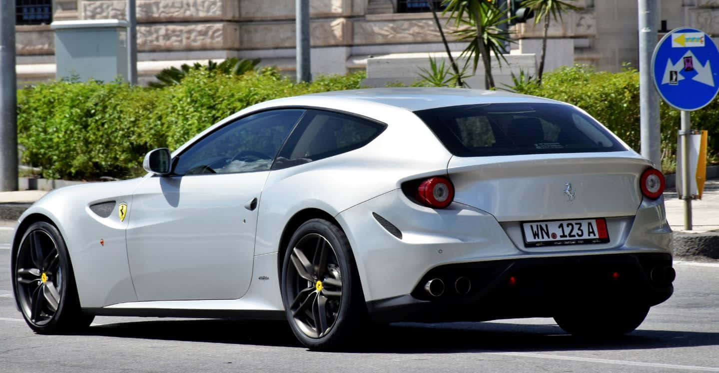 Ferrari Ff 桌布 壁紙 — 一架時尚的白色法拉利FF跑車停泊在陽光明媚的城市街道上，背景有綠色樹籬和石建築。