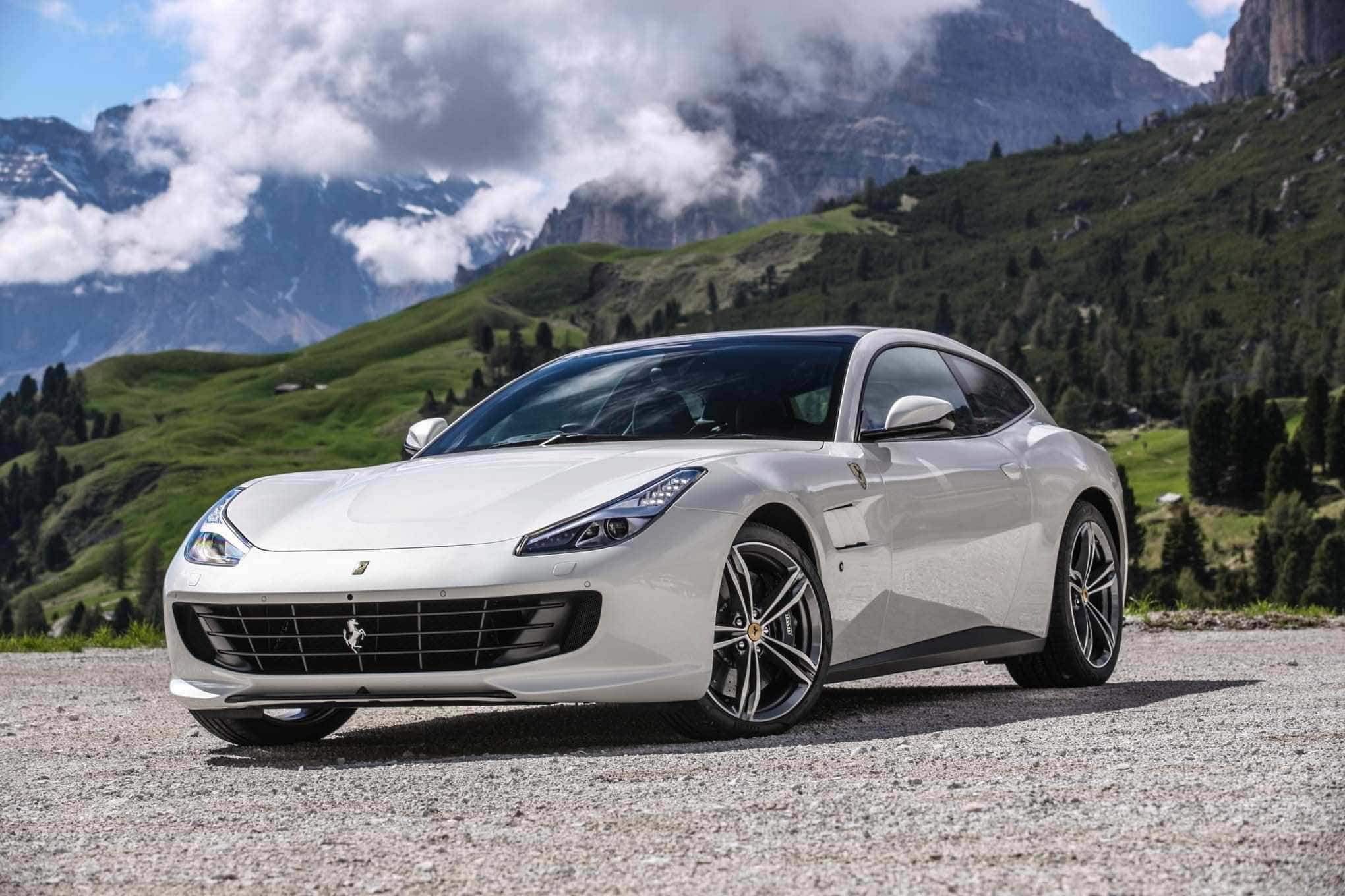 Ferrari Gtc4lusso 桌布 壁紙 — 一架時尚的白色法拉利停泊在碎石路上，背景是雄偉的綠色山脈和雲霧繚繞的山峰。