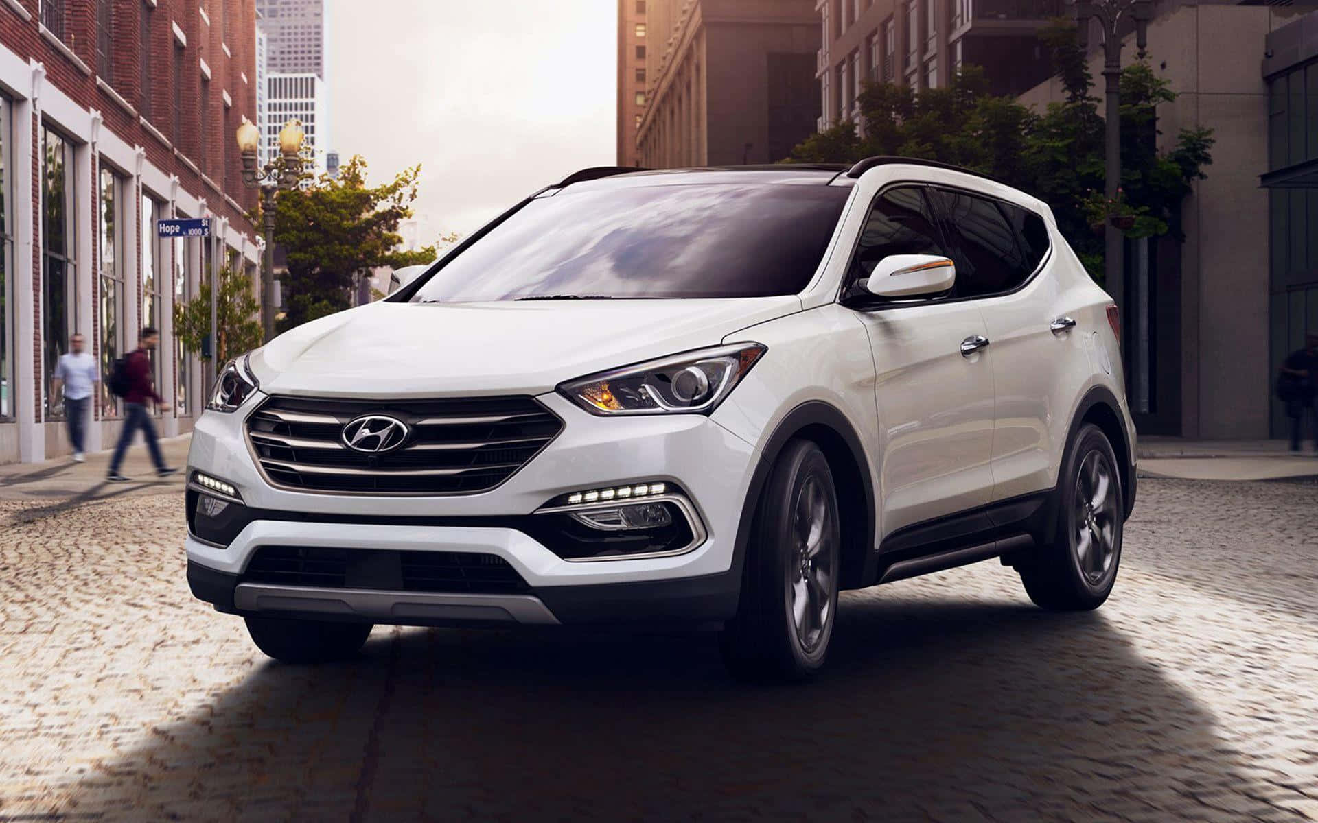 Hyundai Santa Fe 桌布 壁紙 — 一架時尚的白色現代SUV停泊在鵝卵石城市街道上，背景有行人和磚砌建築。