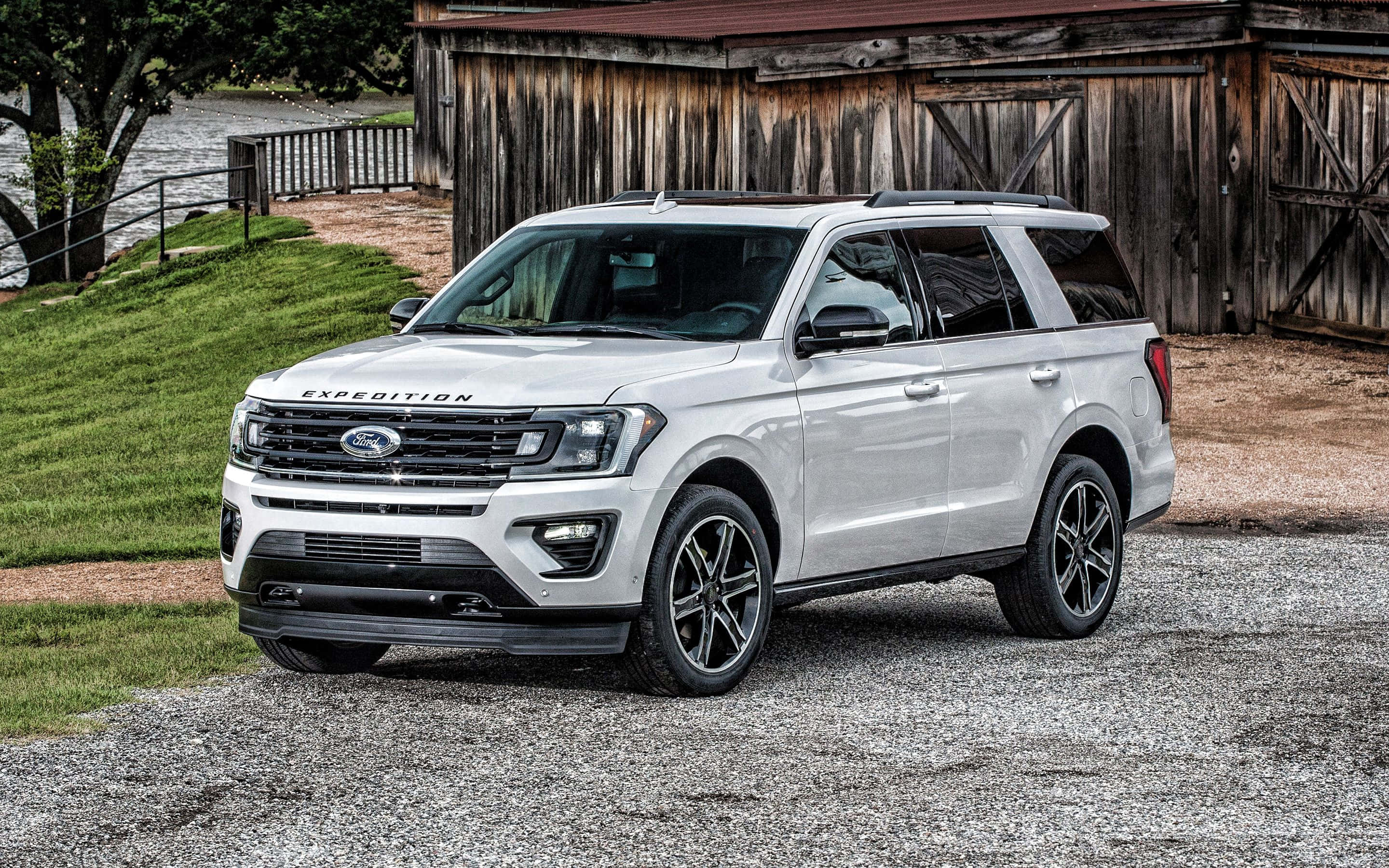 Ford Expedition 桌布 壁紙 — 一架時尚的白色福特 Expedition SUV 停泊在碎石路上，前面是鄉村風格的木製穀倉，背景有綠草和河流。