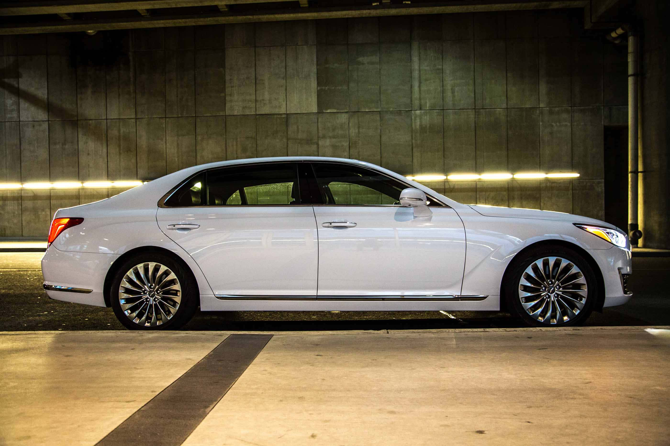 Genesis G90 桌布 壁紙 — 一架時尚的白色豪華轎車停泊在燈光昏暗的地下停車場，周圍是混凝土牆壁和發光的條形燈。
