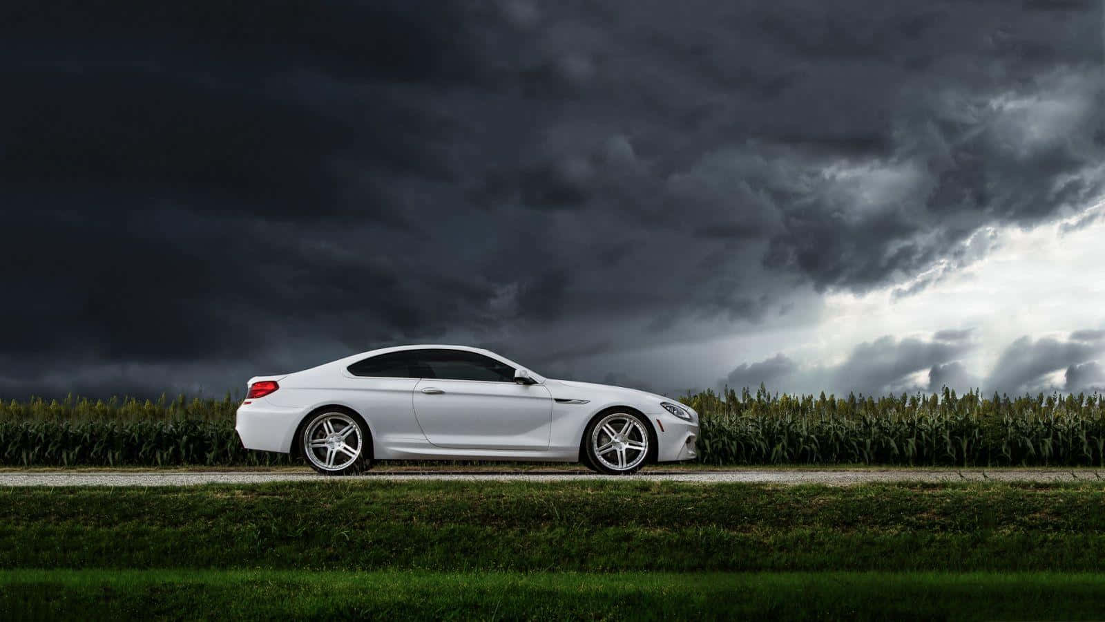 Bmw 6 Series 桌布 壁紙 — 一架時尚的白色跑車停泊在鄉村道路上，頭頂上是戲劇性的暴風雨天空，烏雲密佈。