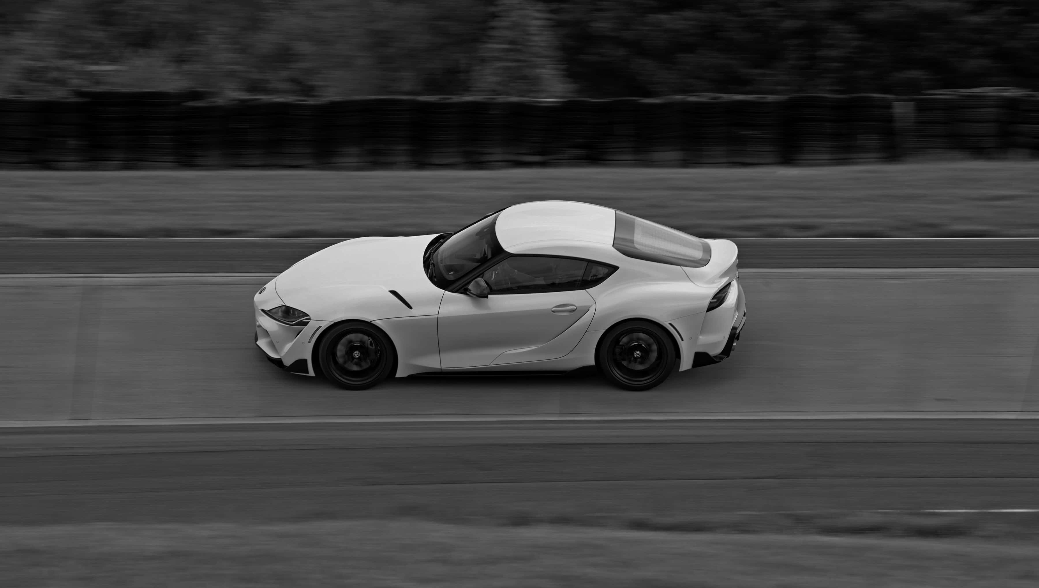 Supra 桌布 壁紙 — 一架時尚的白色跑車在單色調的模糊賽道上疾馳，強調運動感和空氣動力學設計。
