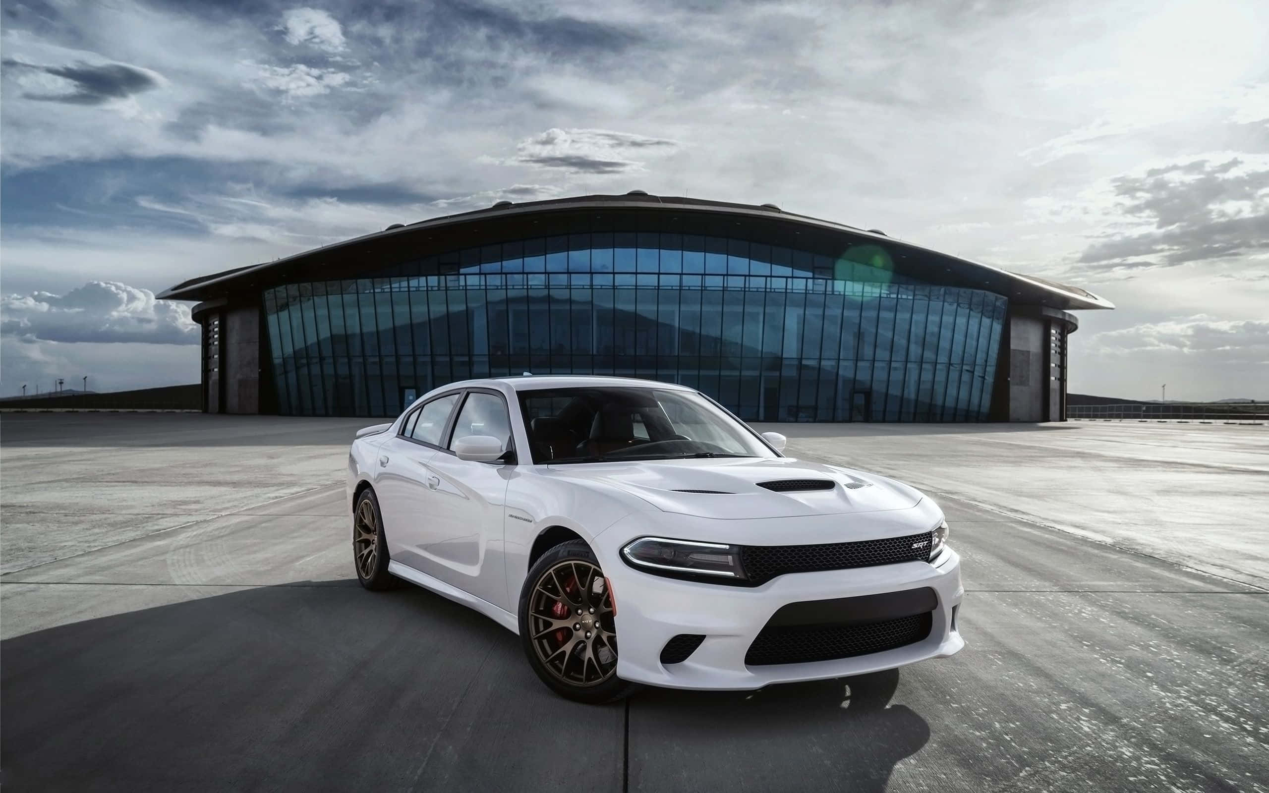 Dodge Charger 桌布 壁紙 — 一架時尚的白色道奇挑戰者停泊在現代玻璃建築前的混凝土廣場上，天空多雲。