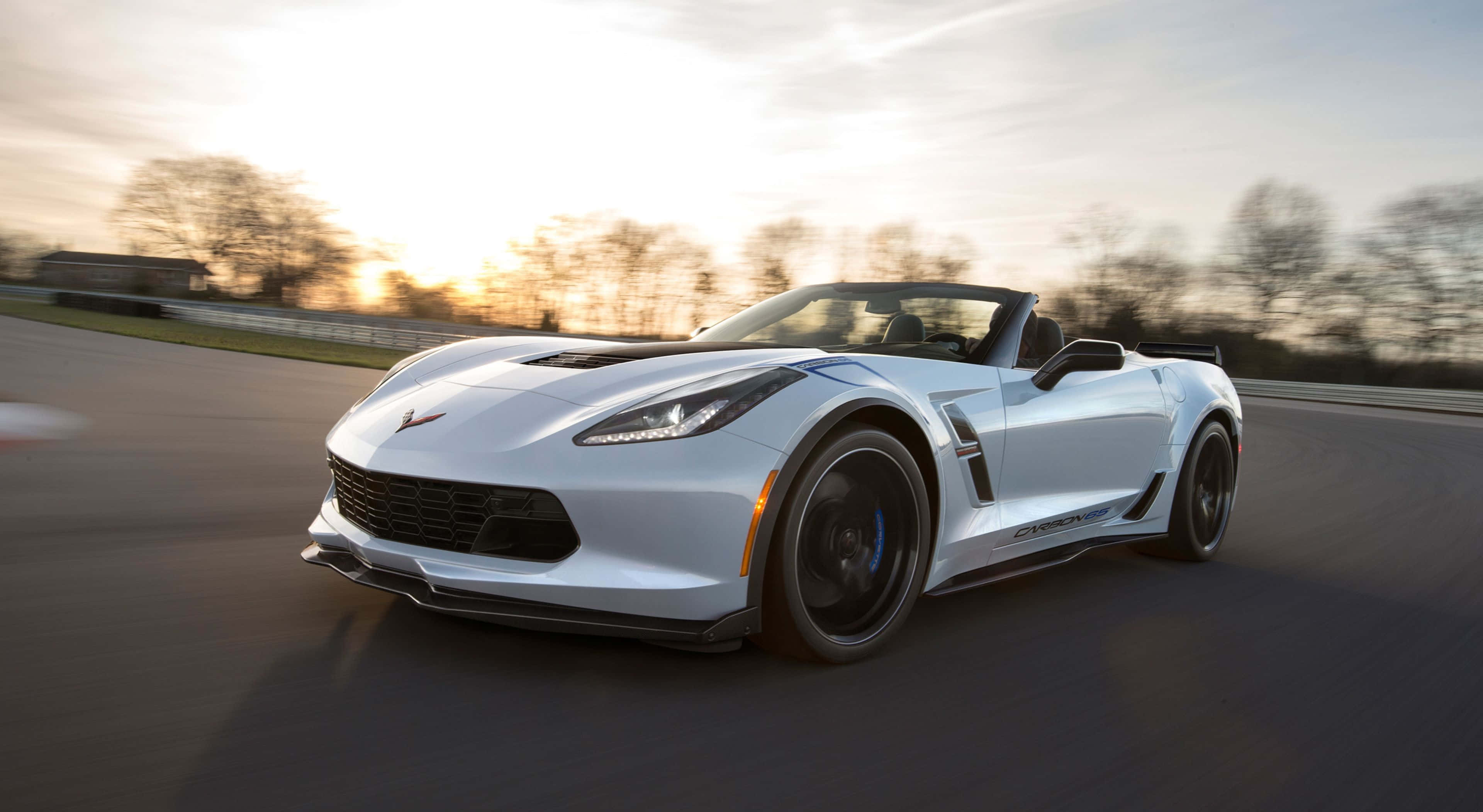 Chevrolet Corvette Grand Sport 桌布 壁紙 — 一架時尚的白色開篷跑車在日落時分沿著賽道飛馳，背景是模糊的樹木。