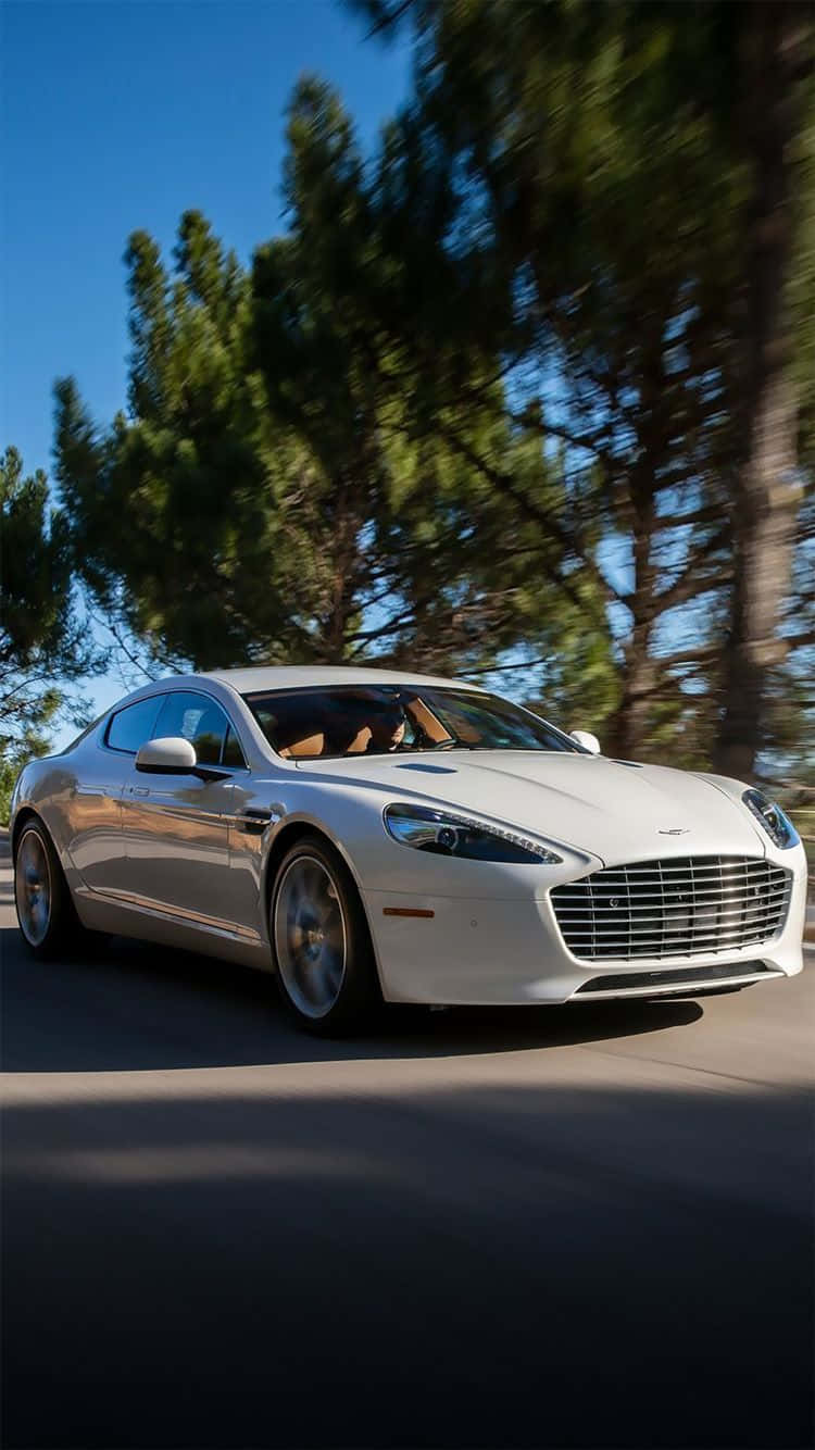 Aston Martin Rapide S 桌布 壁紙 — 一架時尚的白色雅士頓馬田在陽光明媚的道路上飛馳，道路兩旁綠樹成蔭，頭頂是清澈的藍天。