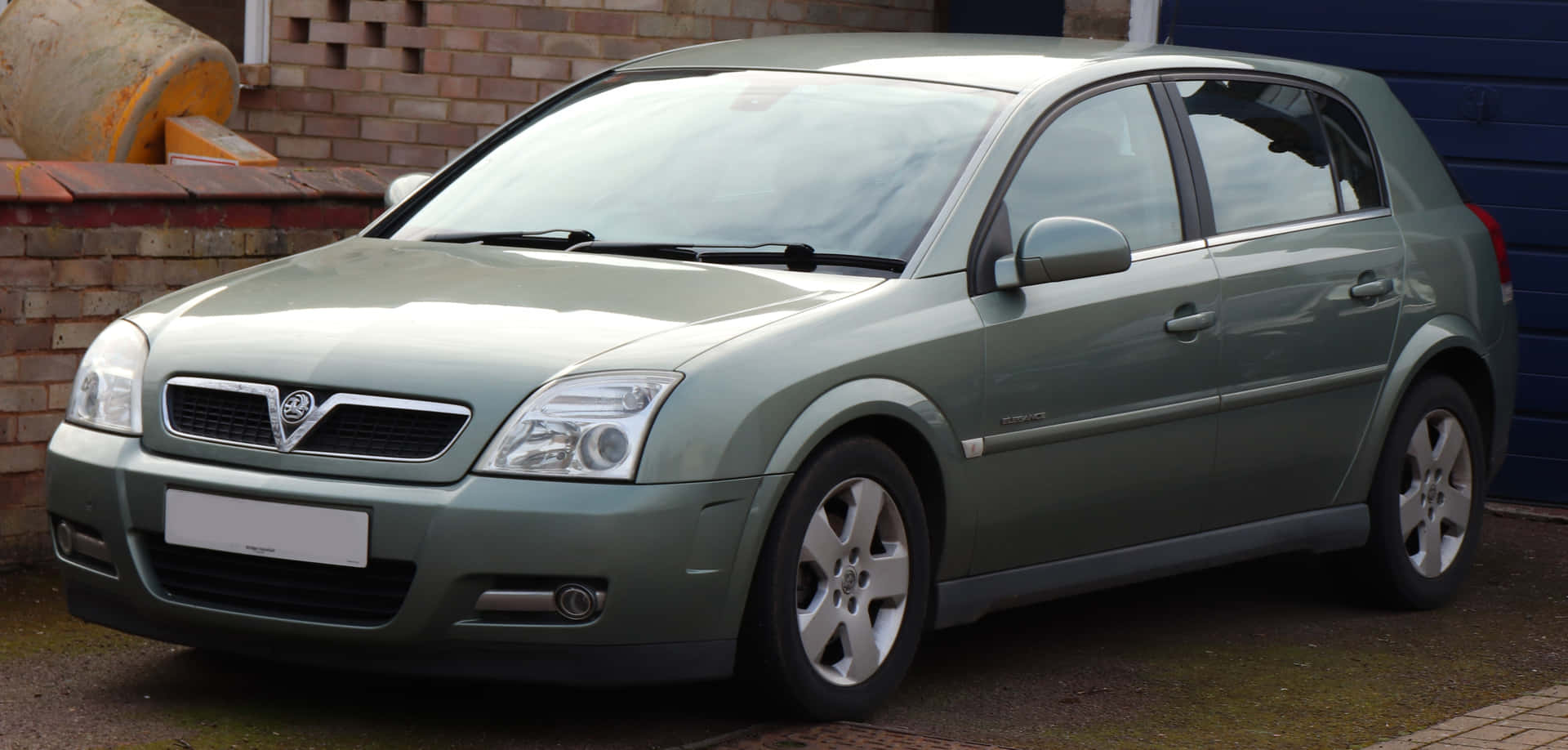  壁紙 — 一架時尚的綠色Vauxhall Vectra掀背車停泊在鋪砌的車道上，旁邊是磚牆和藍色車庫門。