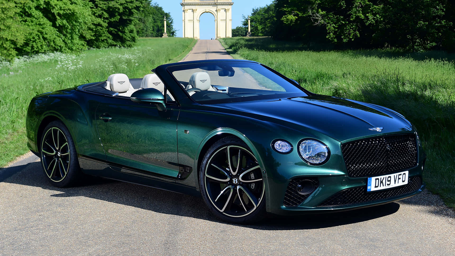 Bentley Continental Gt Convertible 桌布 壁紙 — 一架時尚的綠色賓利開篷車停泊在碎石路上，背景係一個宏偉嘅石拱門，喺明亮陽光下。