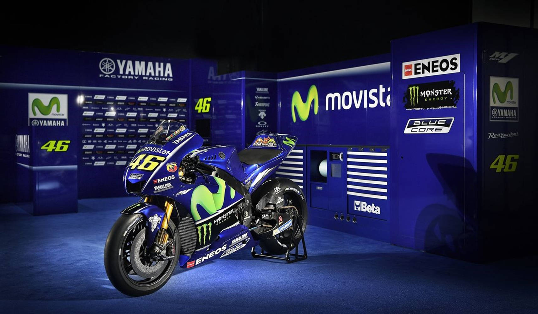 機車 桌布 壁紙 — 一架時尚的藍綠色Yamaha MotoGP賽車，編號46，在明亮的燈光下展示於品牌車庫中。