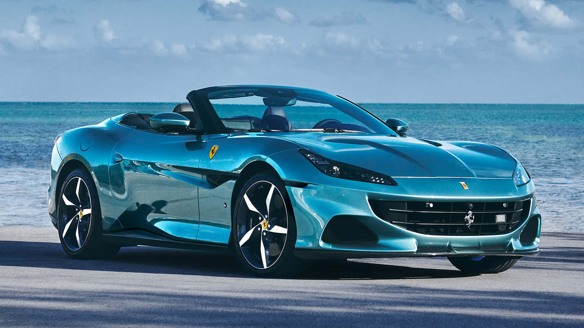 Ferrari Portofino 桌布 壁紙 — 一架時尚的藍綠色法拉利敞篷車在燦爛陽光下，在藍綠色的海浪旁閃閃發光。