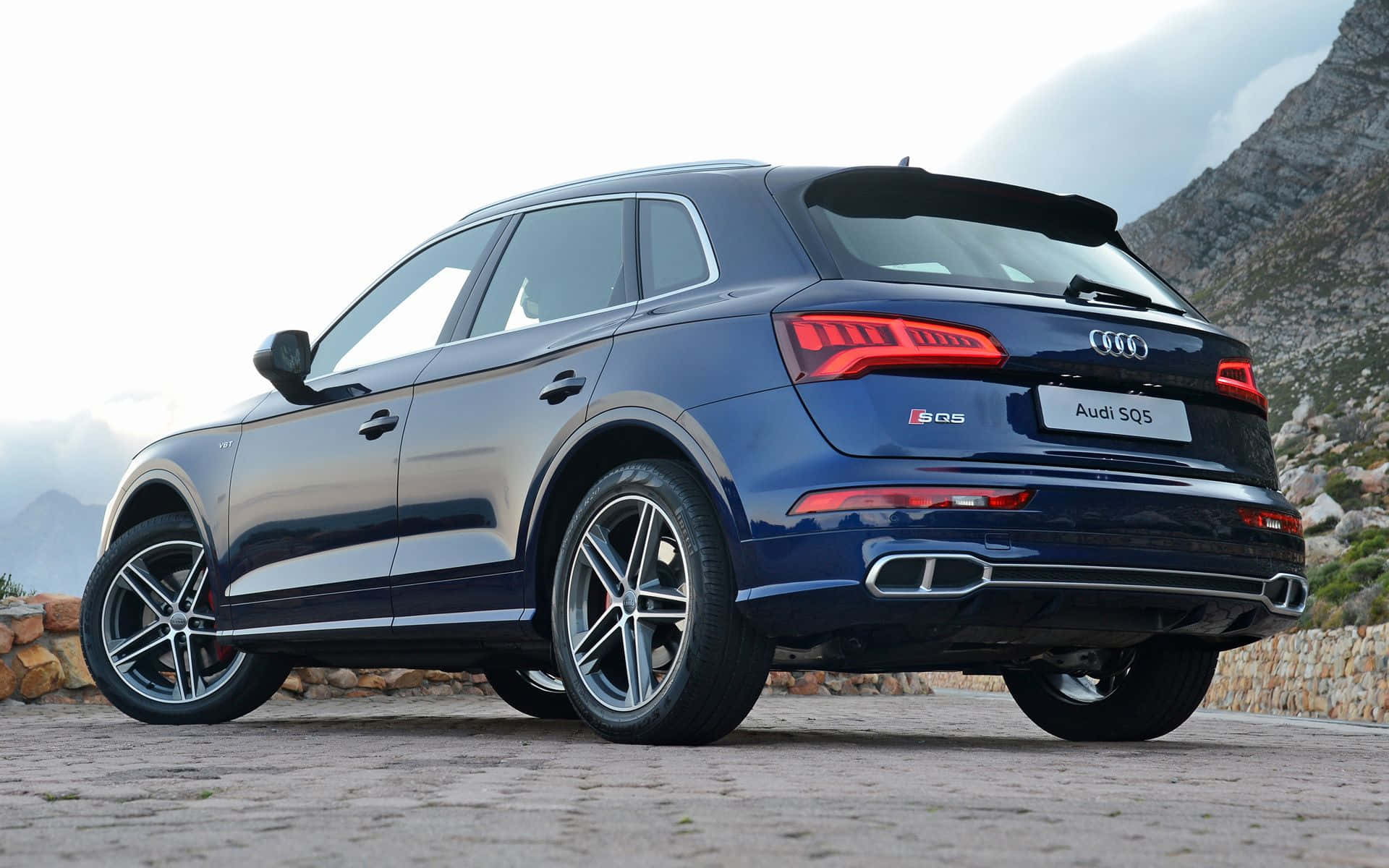 Audi Sq5 桌布 壁紙 — 一架時尚的藍色 Audi SQ5 SUV 停泊在石徑上，背景是崎嶇的山脈，天空多雲。