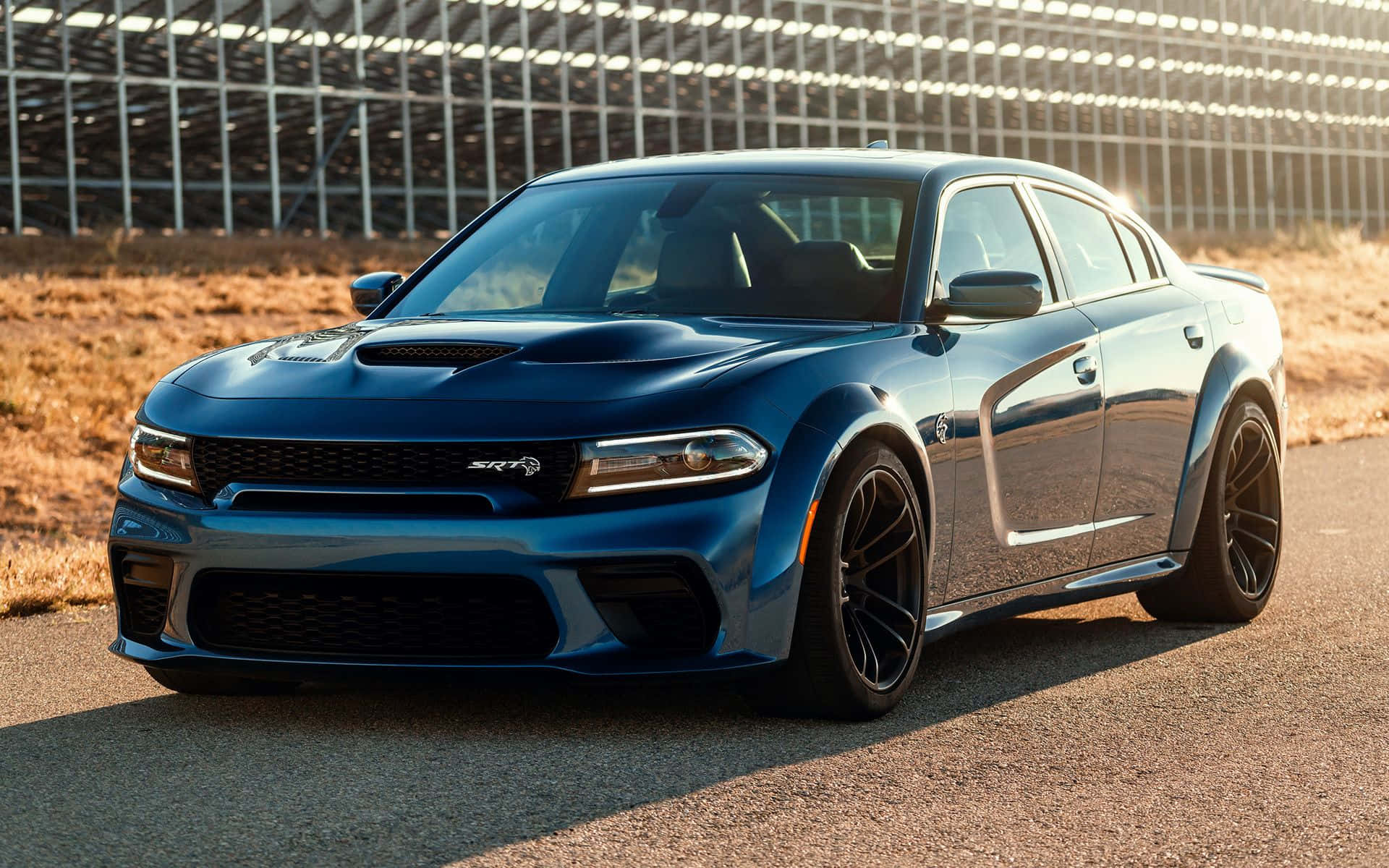 Dodge Charger 桌布 壁紙 — 一架時尚的藍色 Dodge Charger SRT Hellcat 停泊在瀝青賽道上，背景有金屬圍欄和乾草。