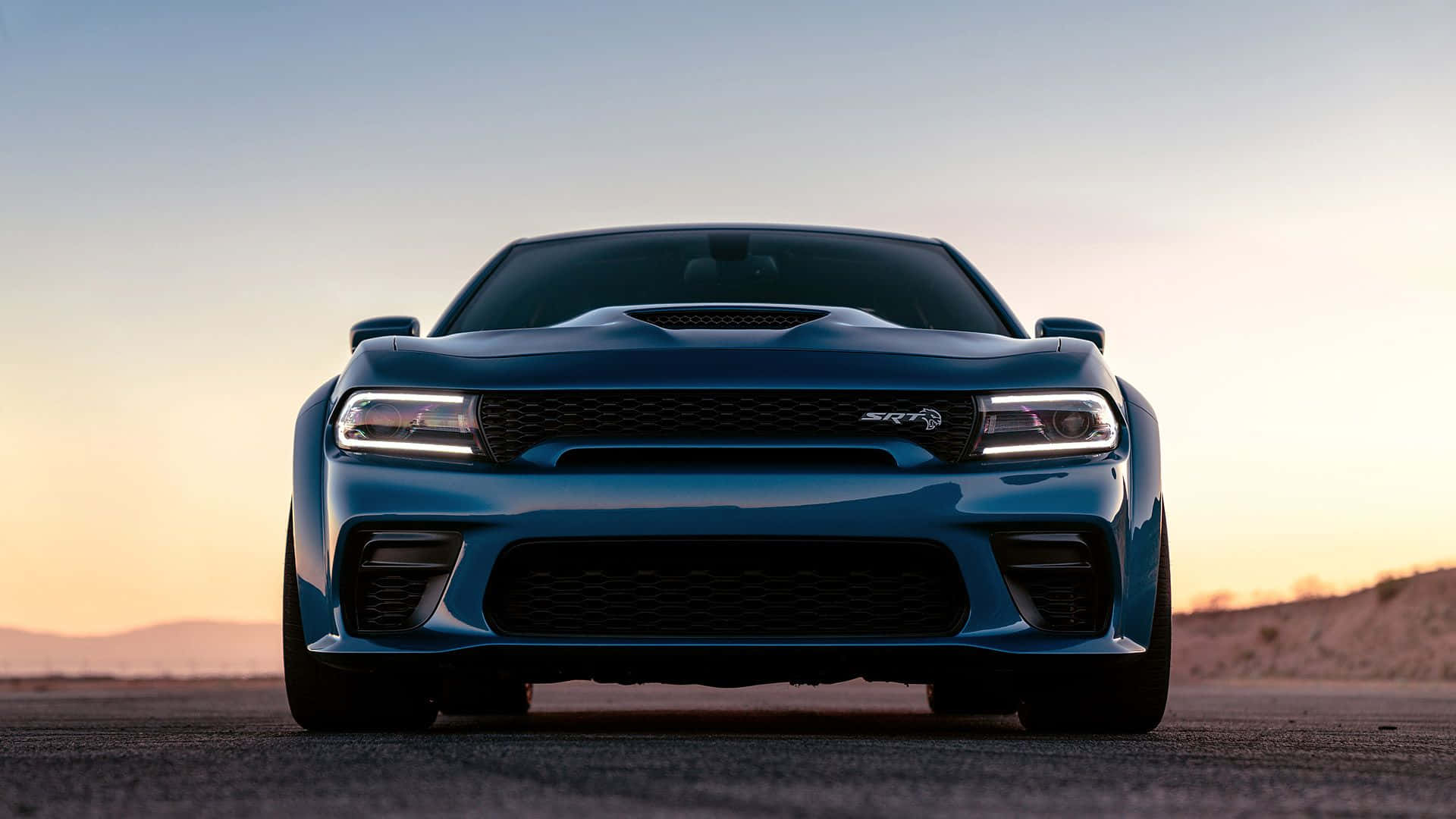 Dodge Charger 桌布 壁紙 — 一架時尚的藍色 Dodge Challenger SRT Hellcat 在日落時分的沙漠公路上向前行駛，天空色調溫暖。