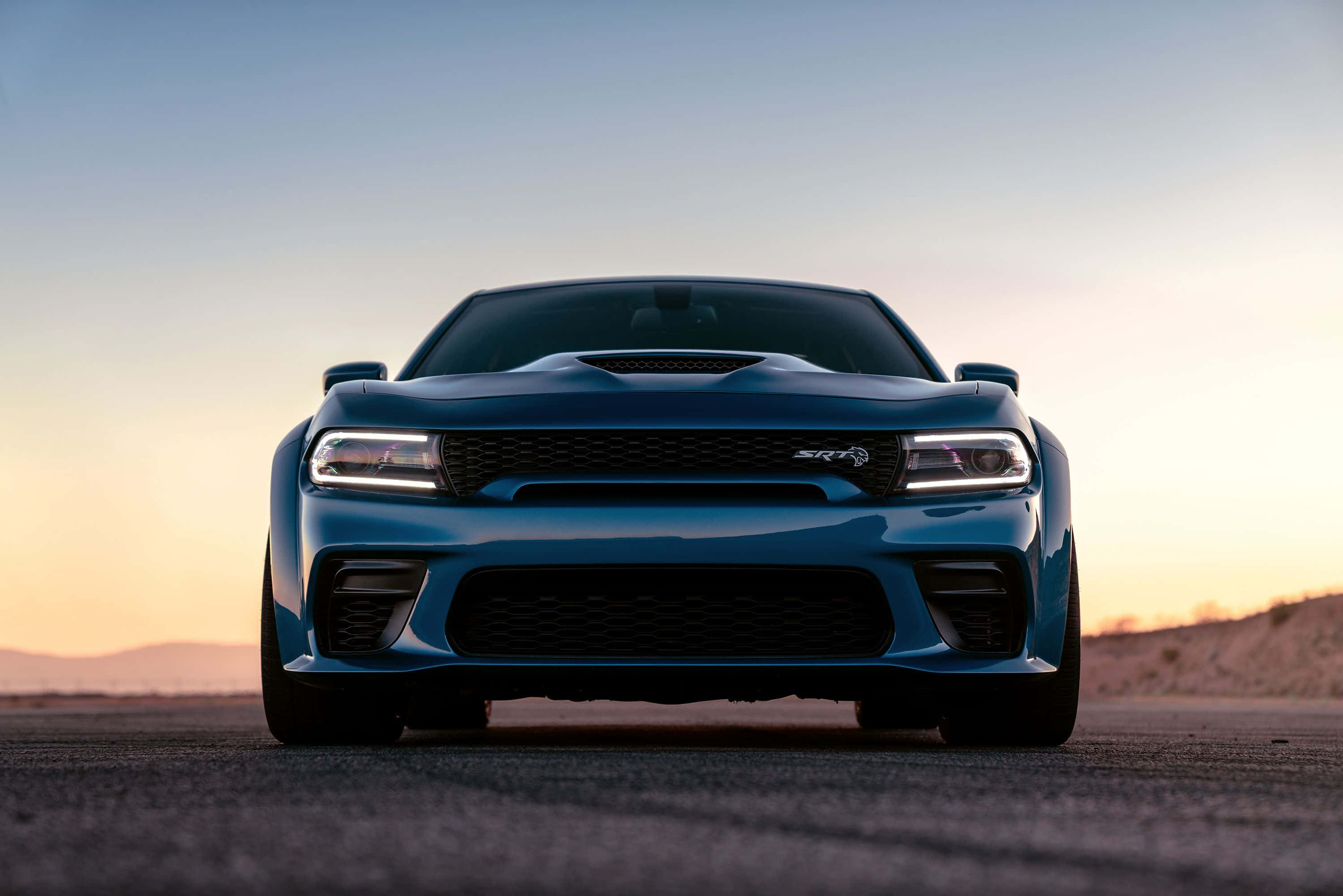 Dodge Charger 桌布 壁紙 — 一架時尚的藍色 Dodge Challenger SRT Hellcat 在沙漠公路上迎著夕陽向前，天空色調溫暖。