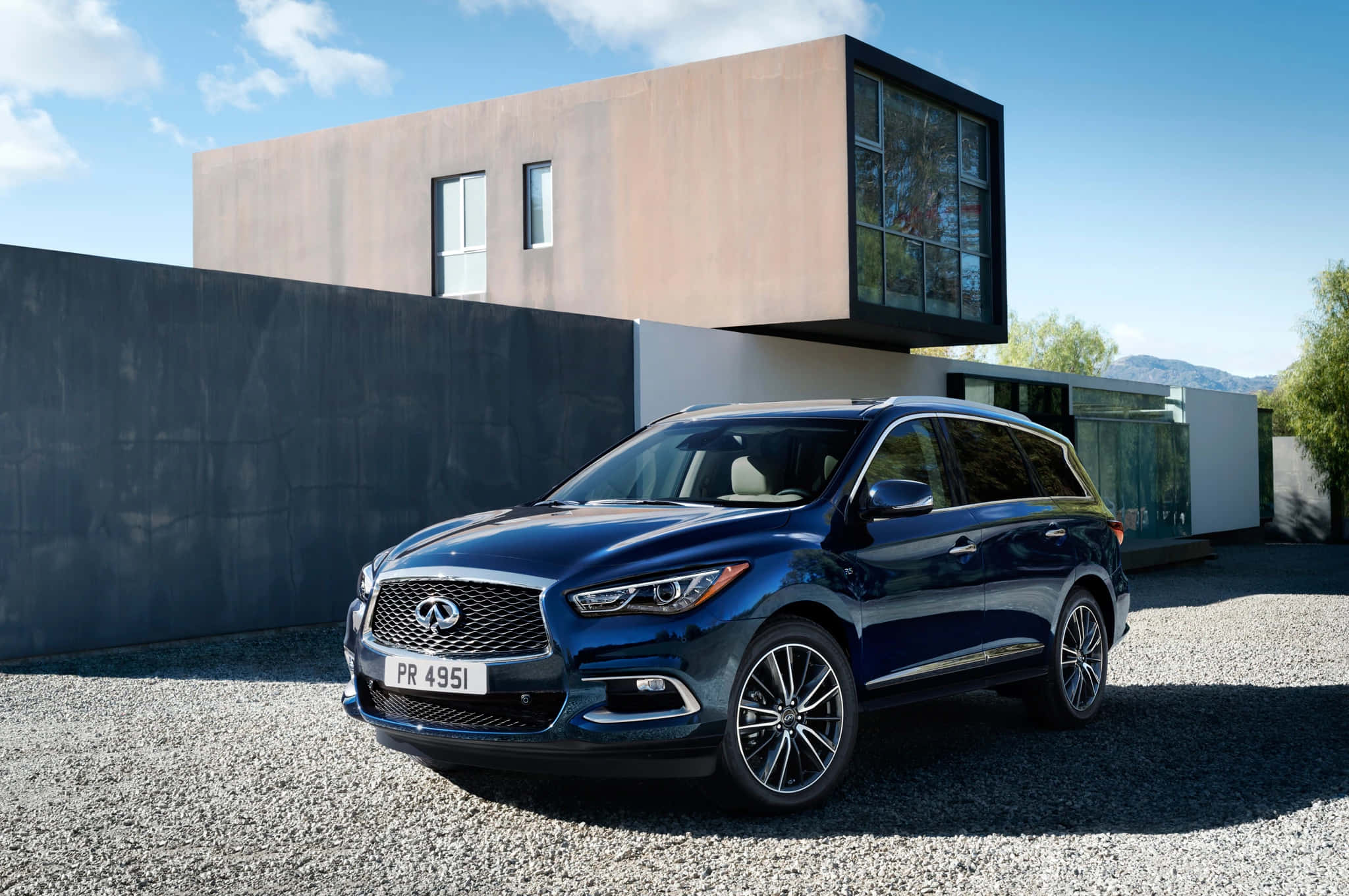 Infiniti Qx60 桌布 壁紙 — 一架時尚的藍色 Infiniti QX60 SUV 停泊在碎石路上，前方是一座現代簡約風格的房屋，背景是清澈的藍天。
